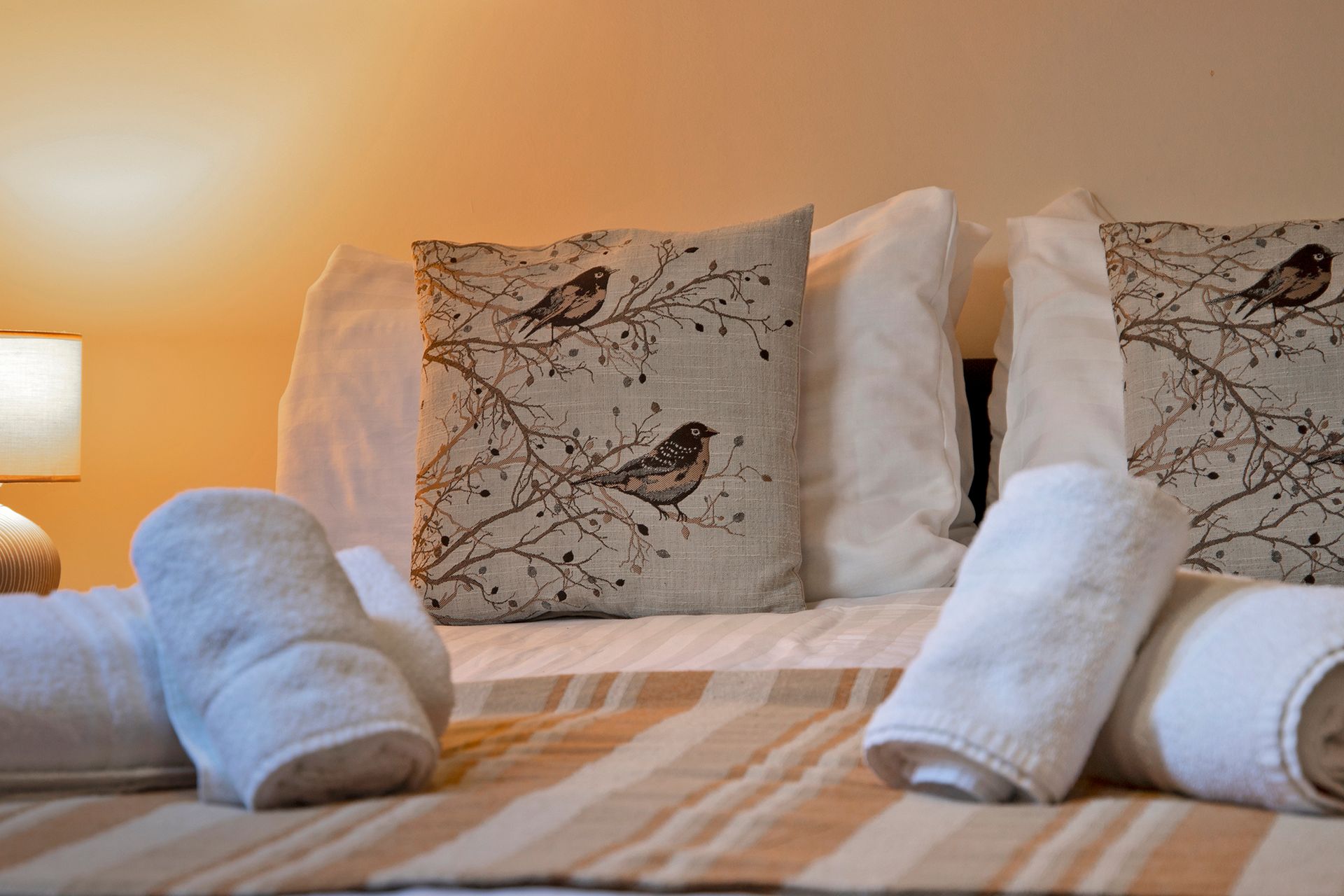 A bed with rolled towels, pillows and bird cushions and lamp