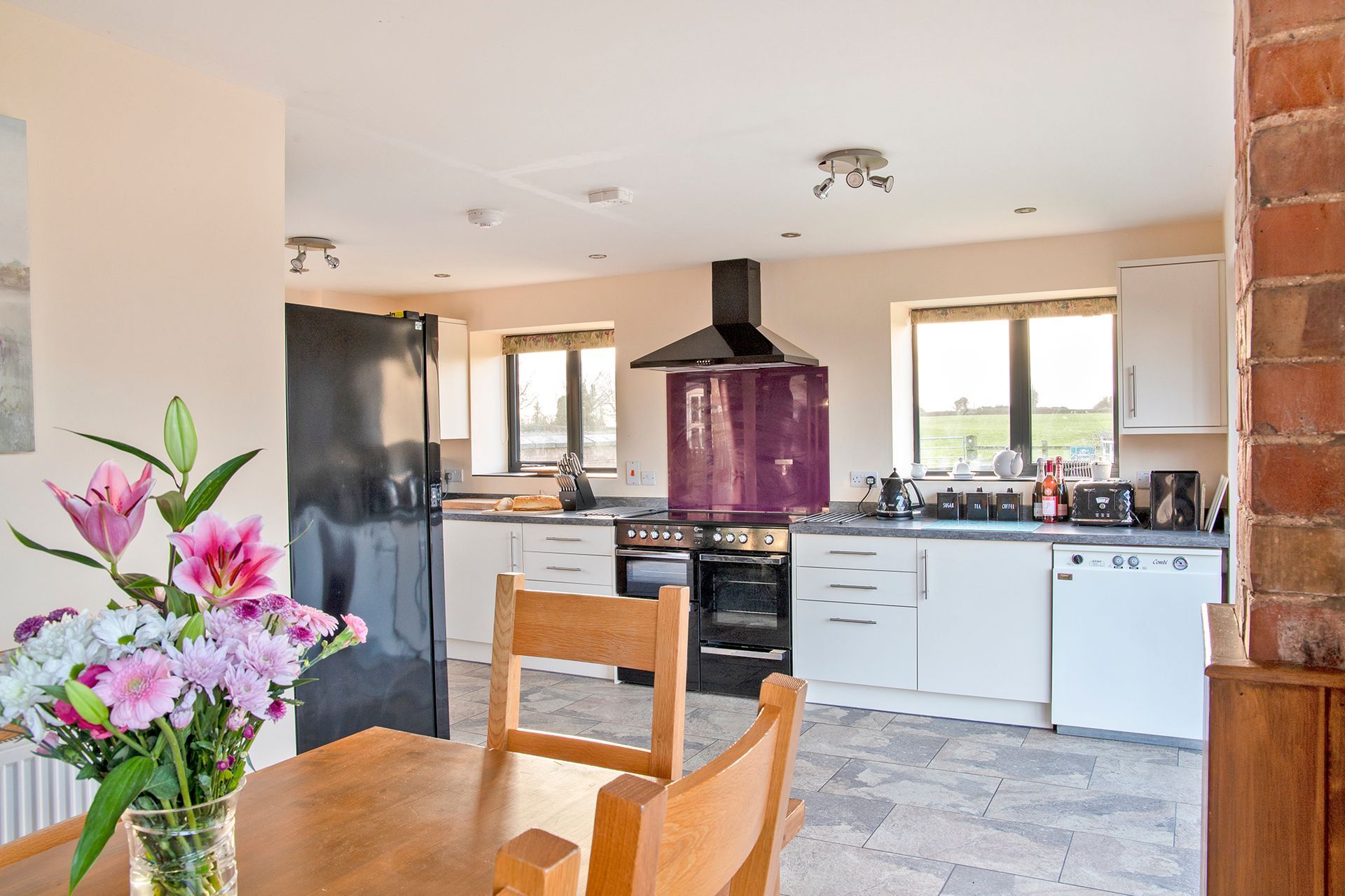 Vase of flowers on dining table with kitchen in the back ground with range cooker