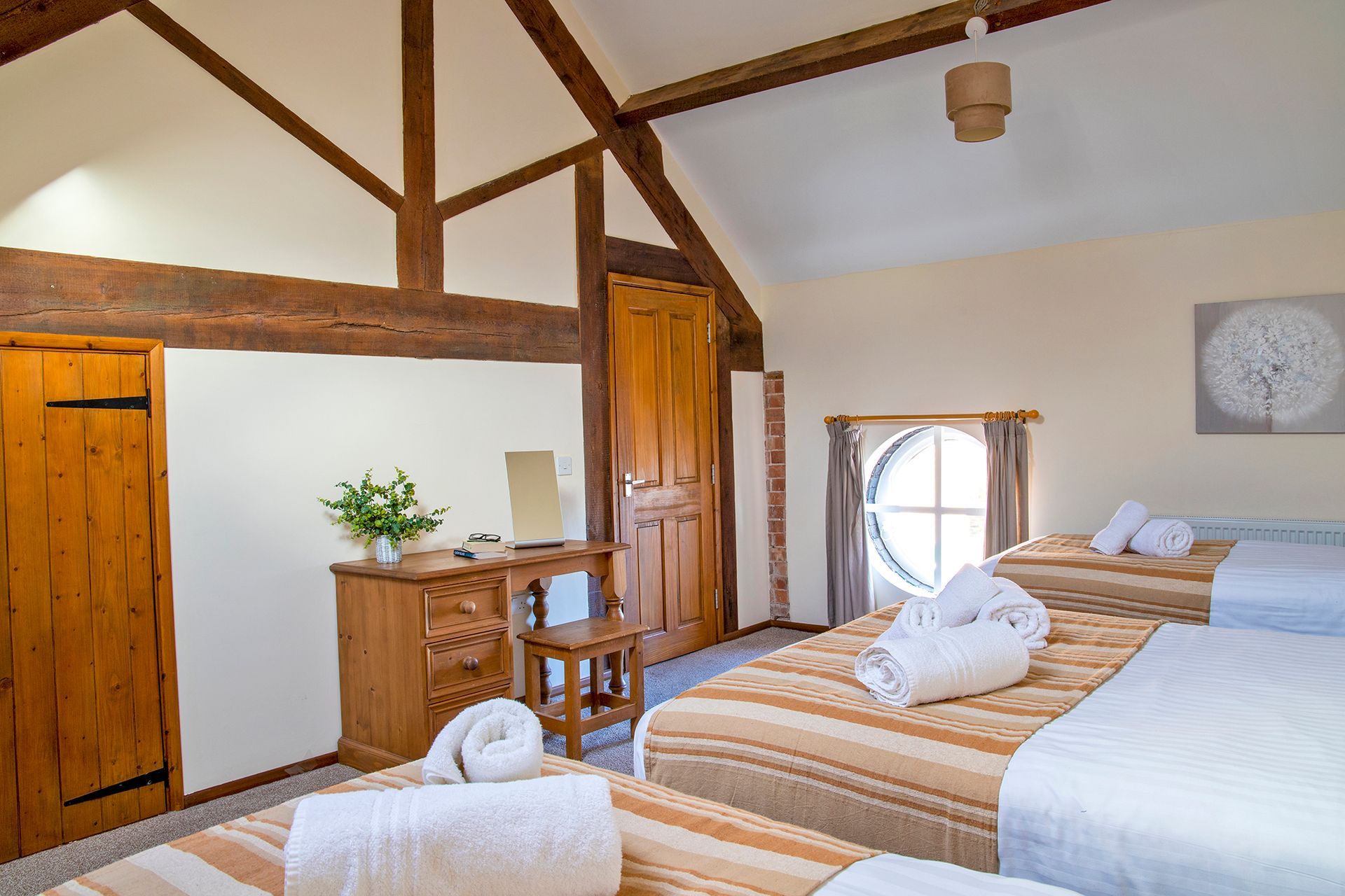 Bedroom with oak beams and a round window and wooden dressing table