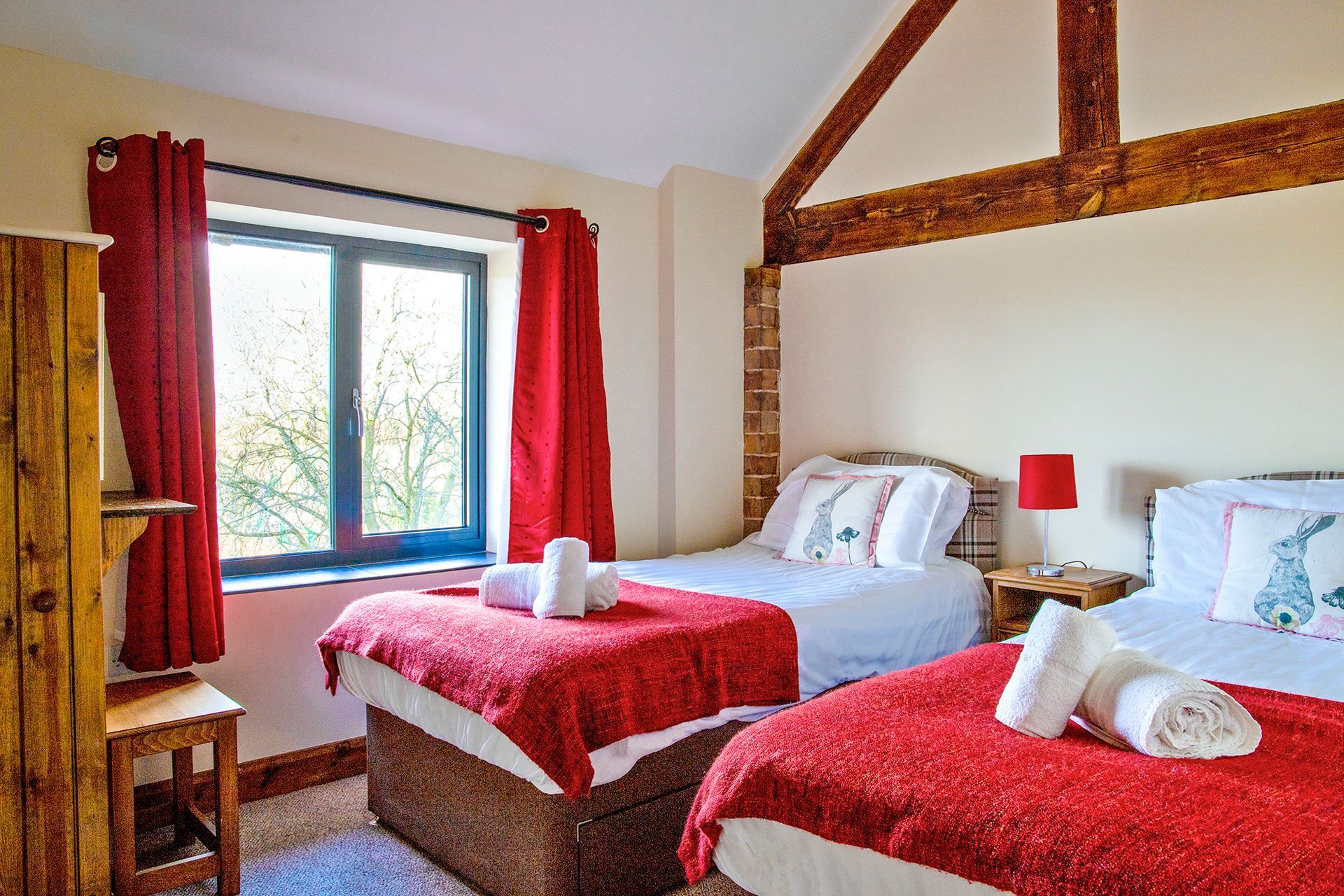 Twin bedroom with beams, red throw and rabbit cuhsions