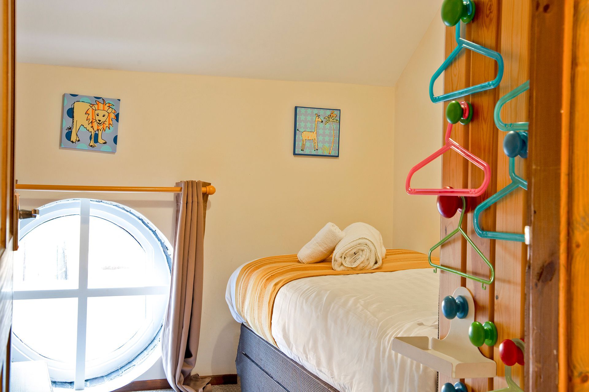 A child's single bedroom with plastic hangers and round window