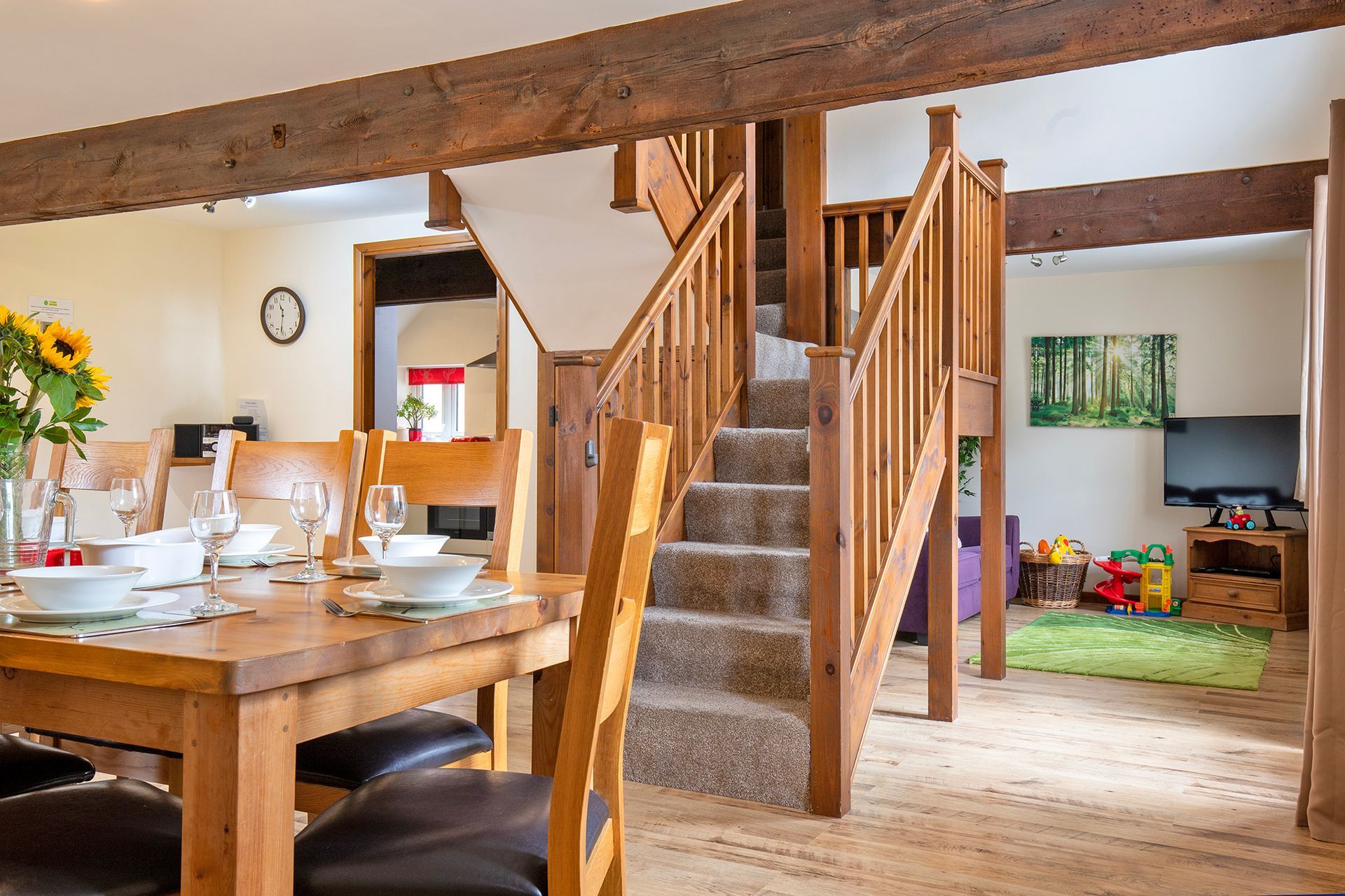 Open plan cottage with wooden staircase, laid dining table with wine glasses and sun flowers