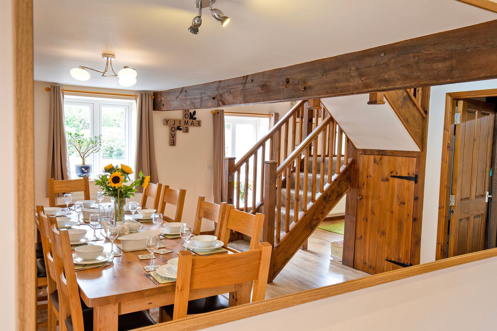 Wooden dining table laid with white china, glasses, wooden staircase, oak beams
