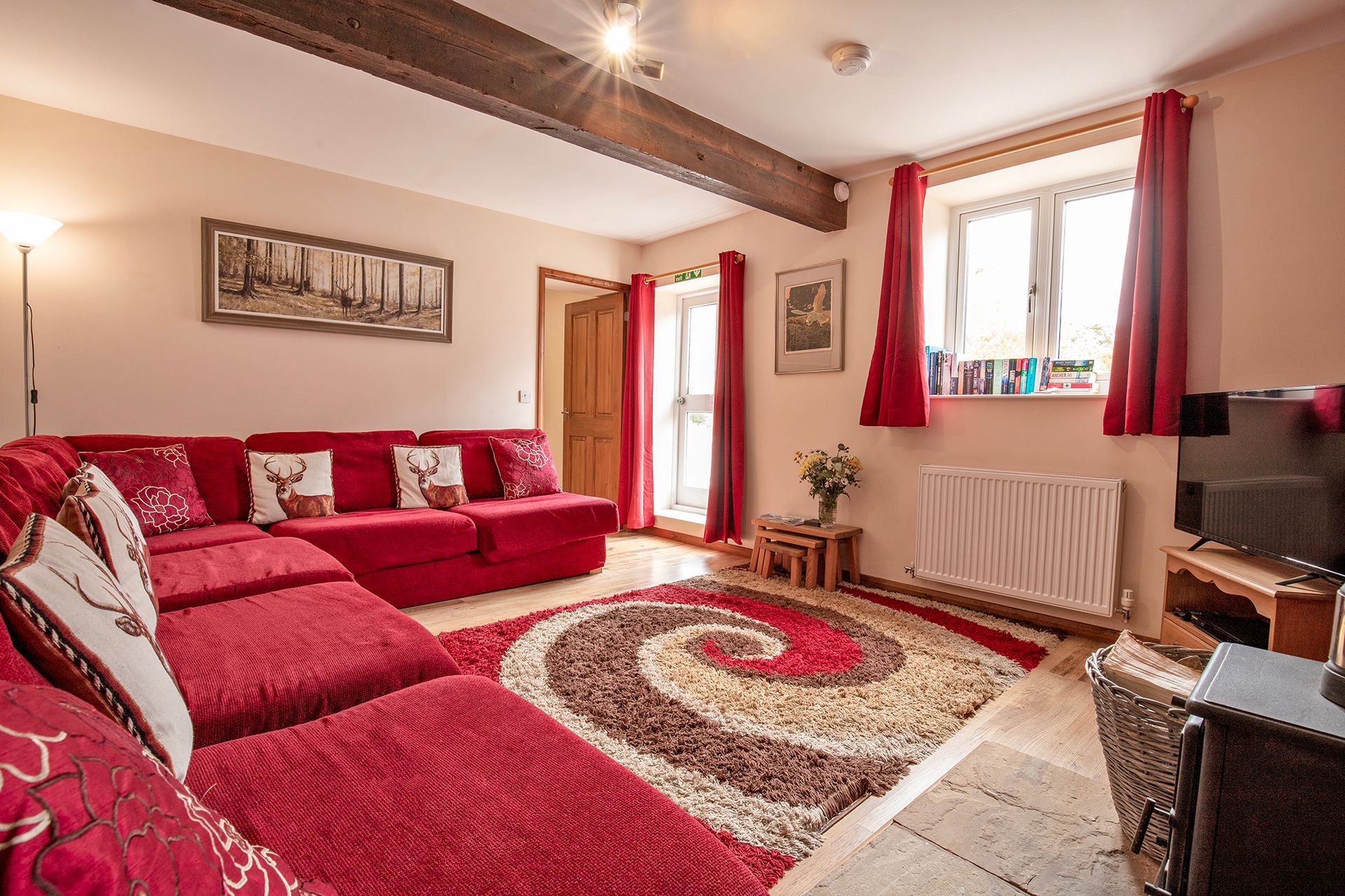 Sitting room with red sofa and stag cushions, bright sunshine coming through the windows