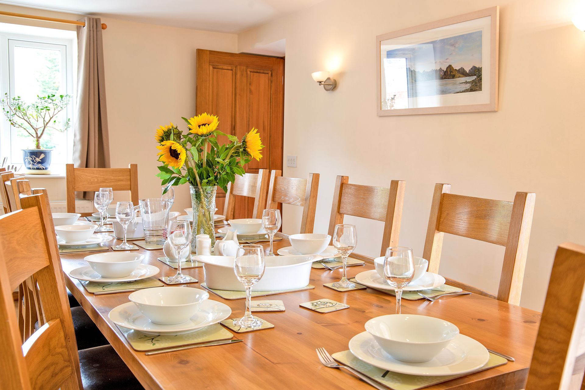Laid dining table and chairs with white china, wine glasses and a vase of sunflowers