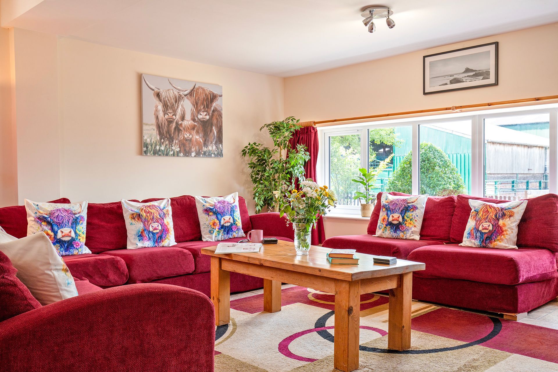 Red sofas with cushions with west highland cattle on a large coffee table with a bunch of flowers