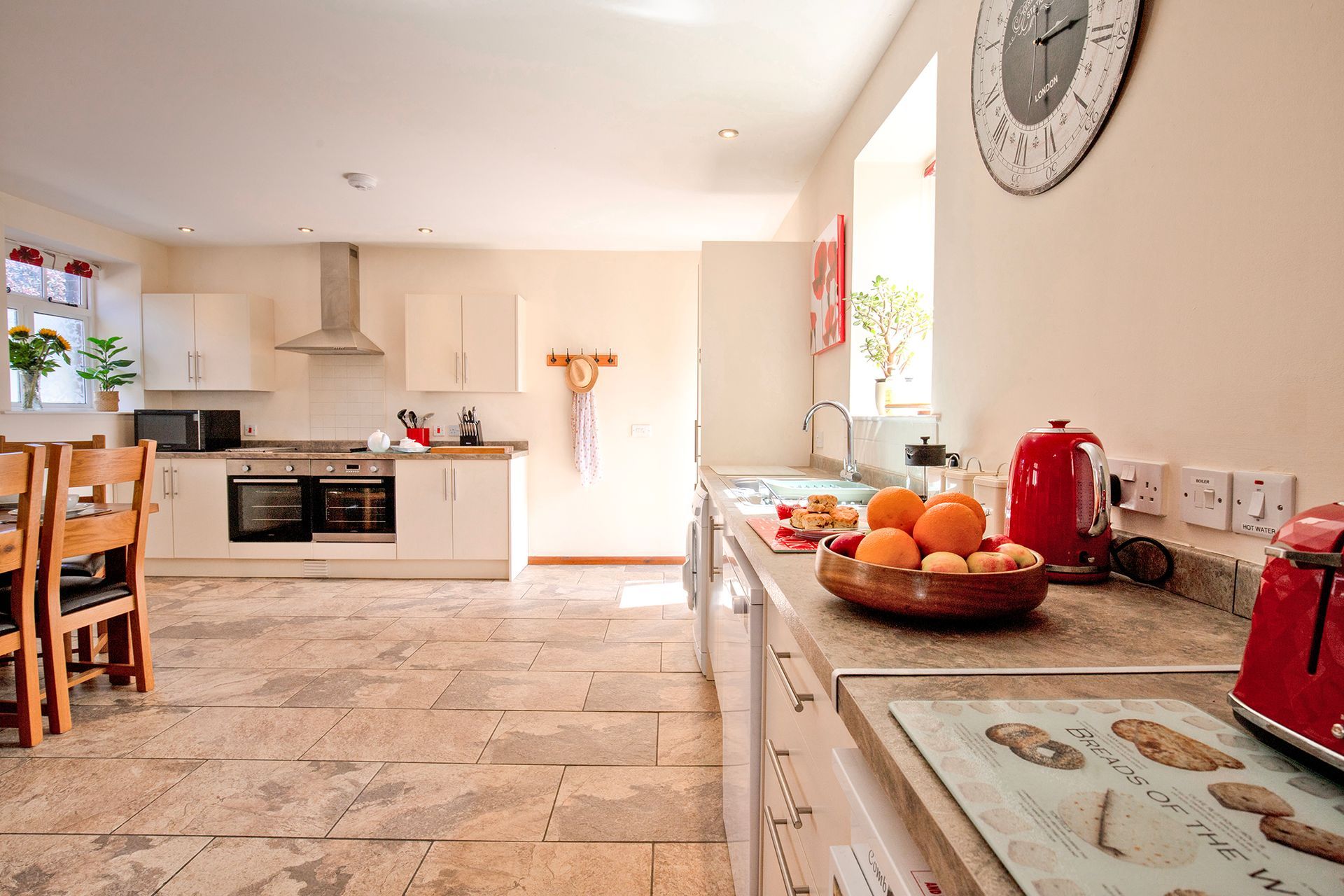 Open plan modern kitchen with a fruit bowl, red kettle and stone floor