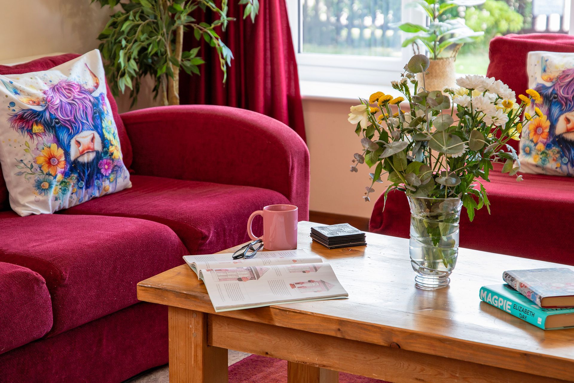 Red sofa with cushions with highland cattle on and a large vase of flowers on a coffee table