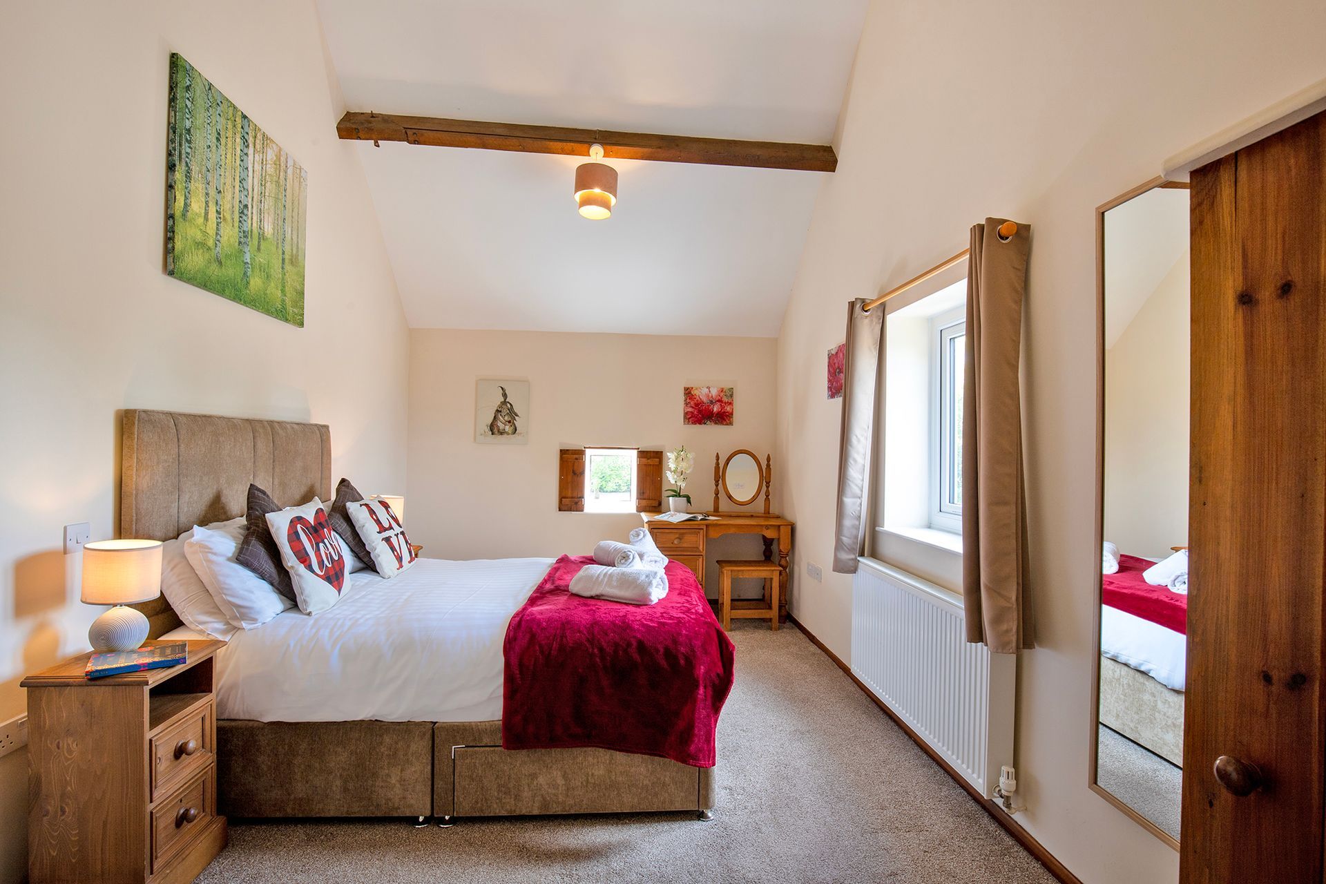 Double bedroom with wooden dressing table, red throw and oak beams