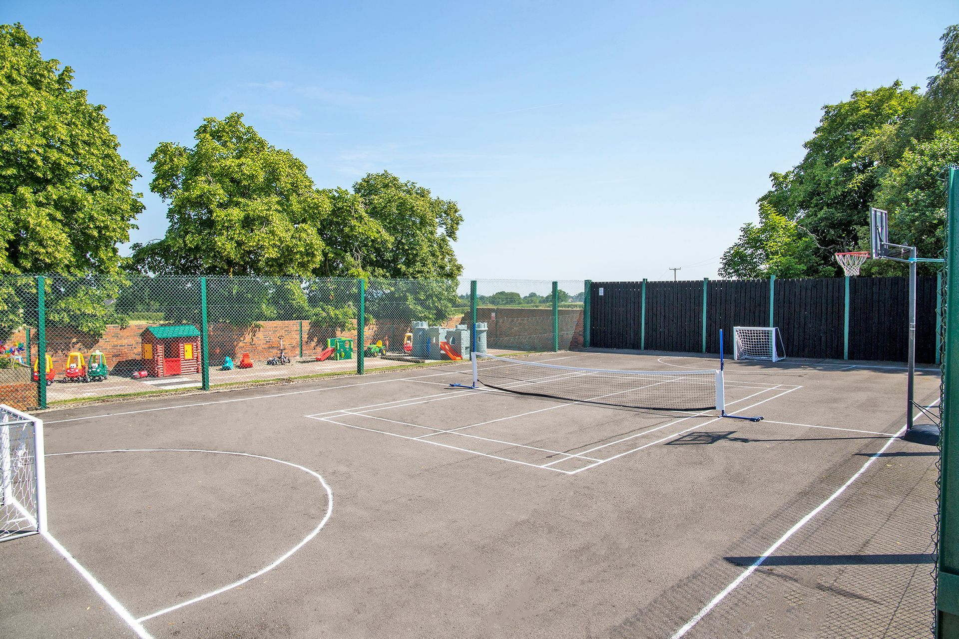 Sports court with tennis net, basketball net and small football nets with a play area on a sunny day