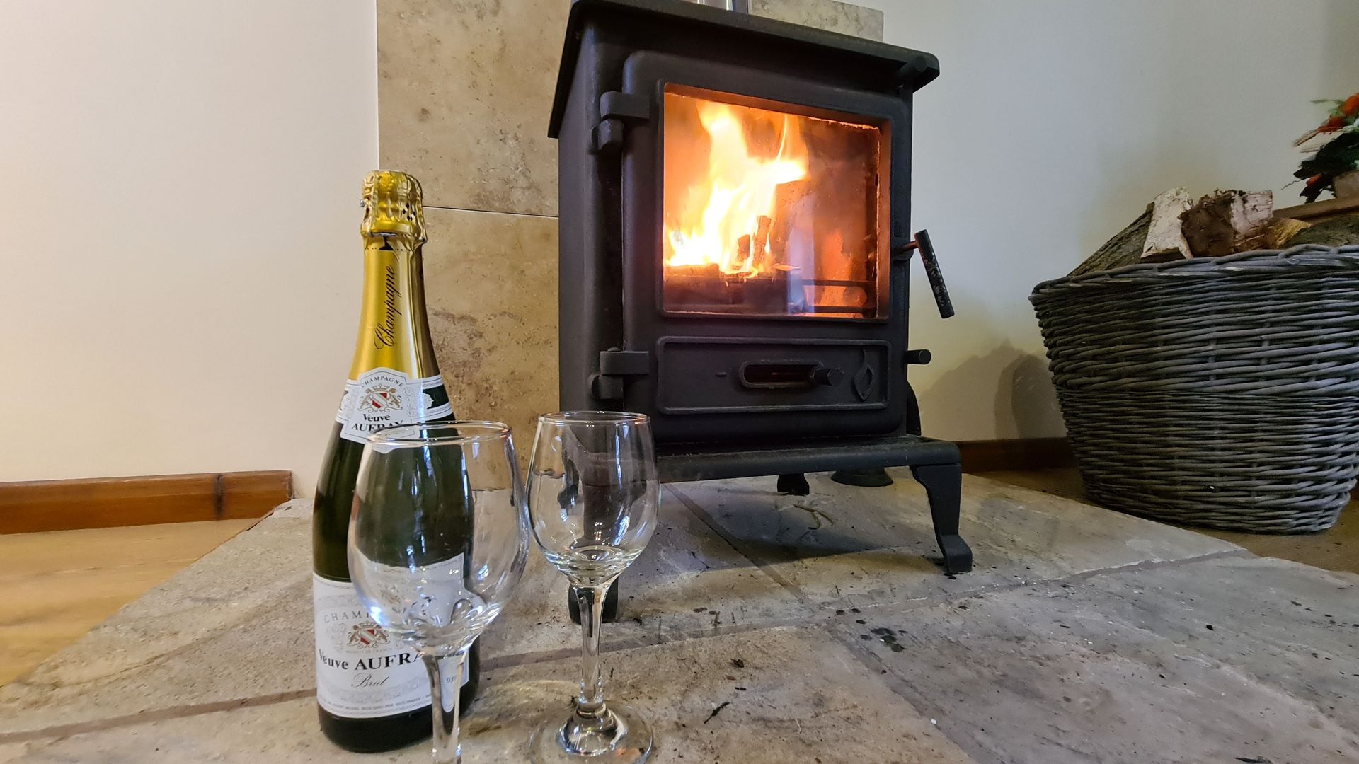 A lit Woodburning stove with a basket of wood and champagne and glasses