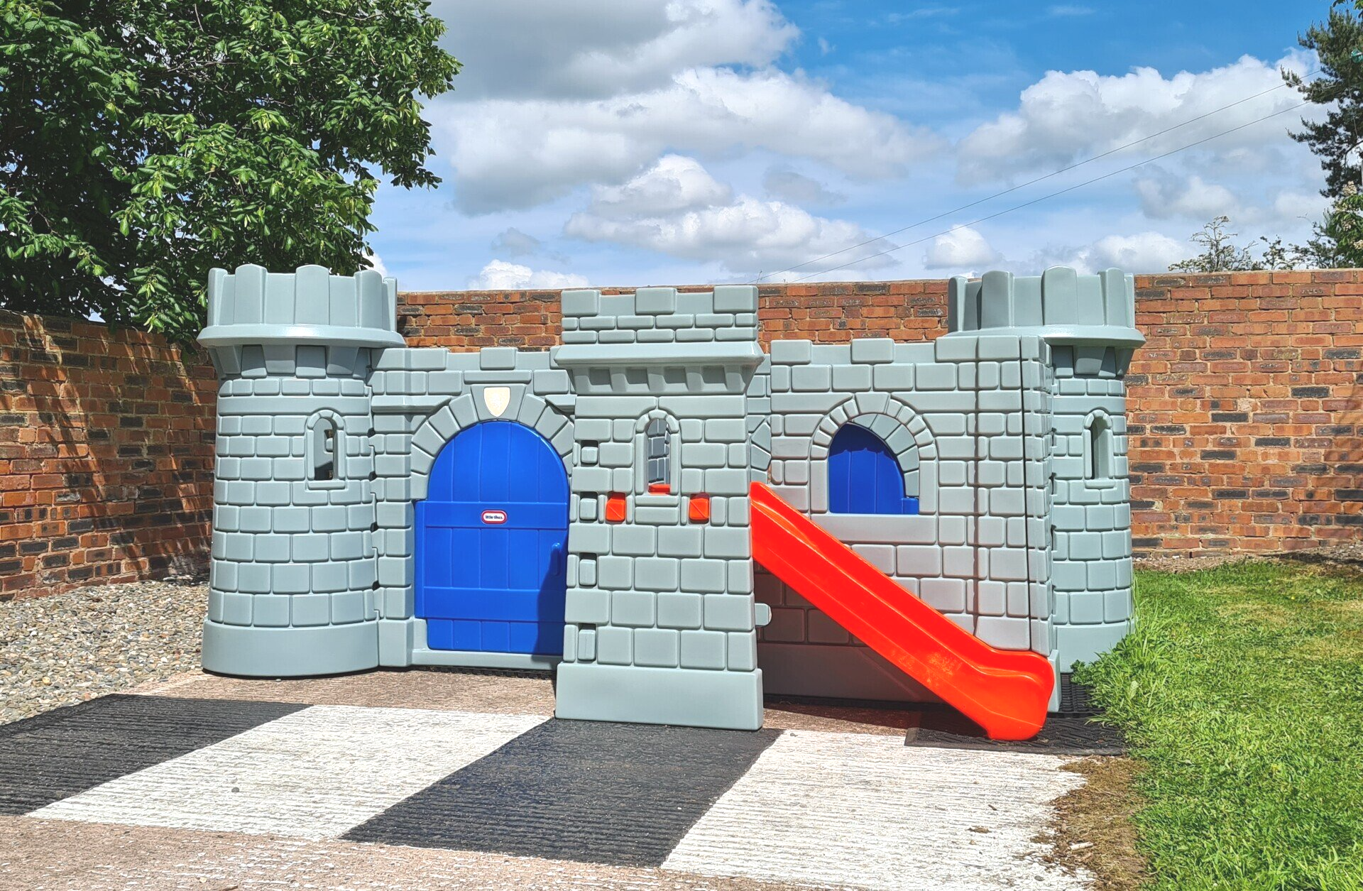 Grey plastic play castle with orange slide on a sunny day