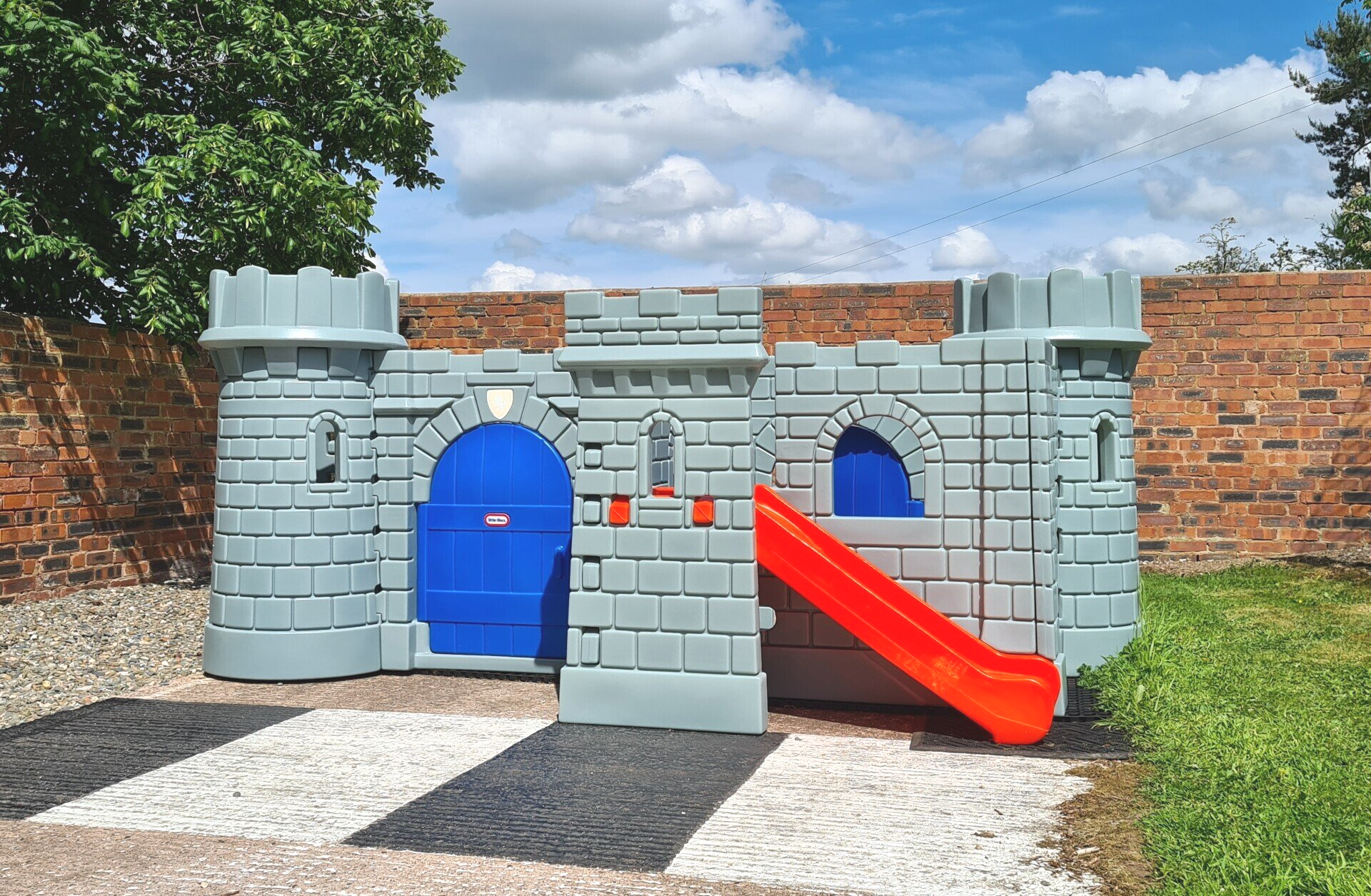 a grey play castle with orange slide outside