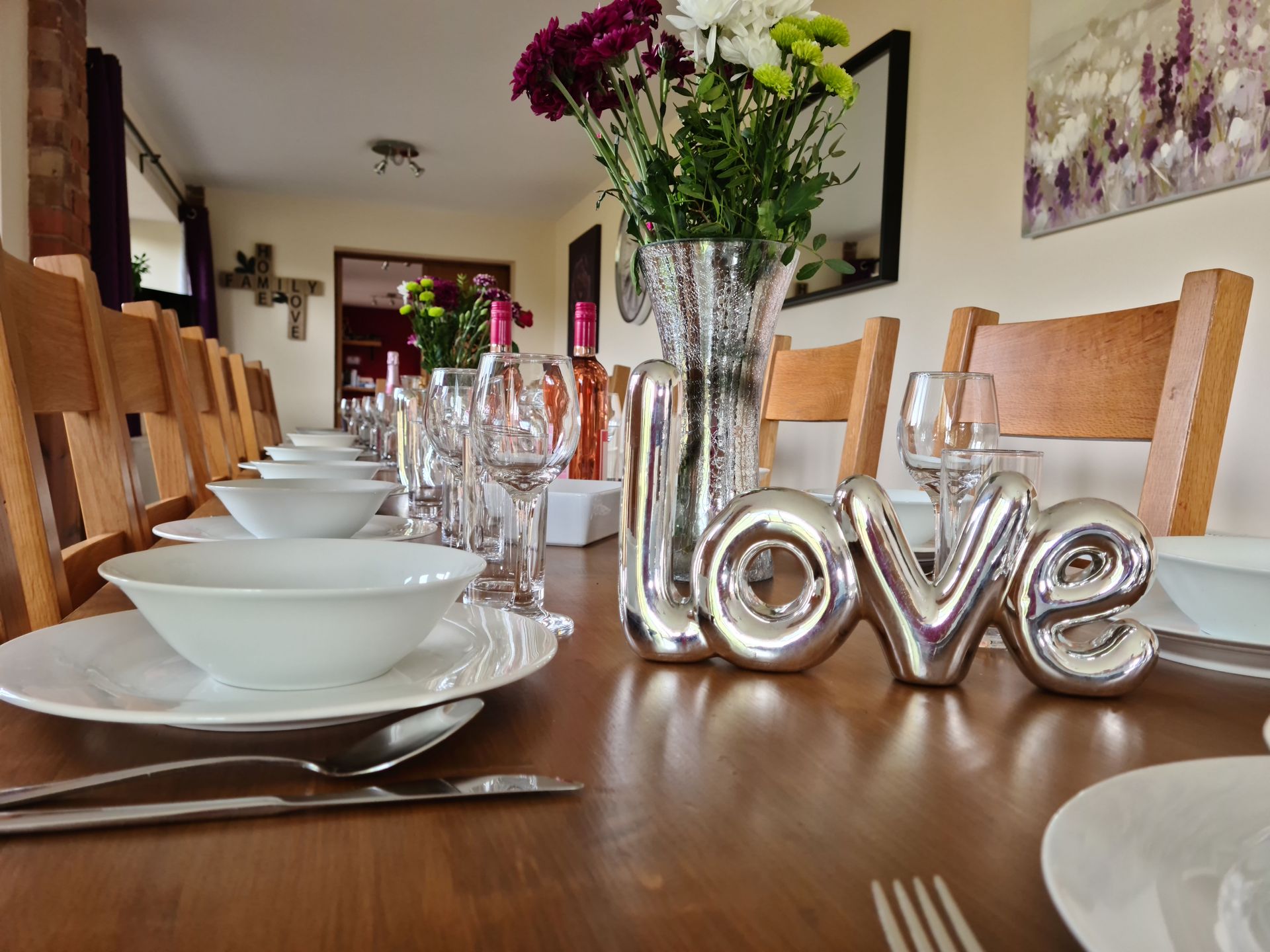 A laid dining table with white china, wine glasses, flowers and wine