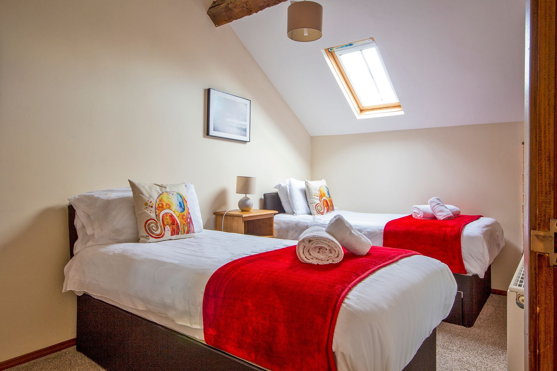Twin bedroom with white linen, elephant cushions and red blankets and rolled white towels