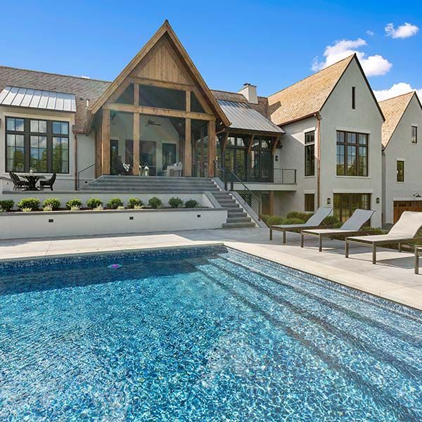 Modern house with large backyard pool, lounge chairs, and a glass-front patio under a blue sky