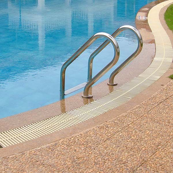 Curved stainless steel pool ladder beside a blue swimming pool with textured tan coping