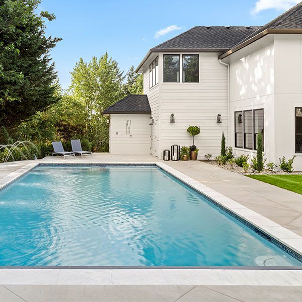 Backyard pool beside a modern white house with patio lounge chairs and trees