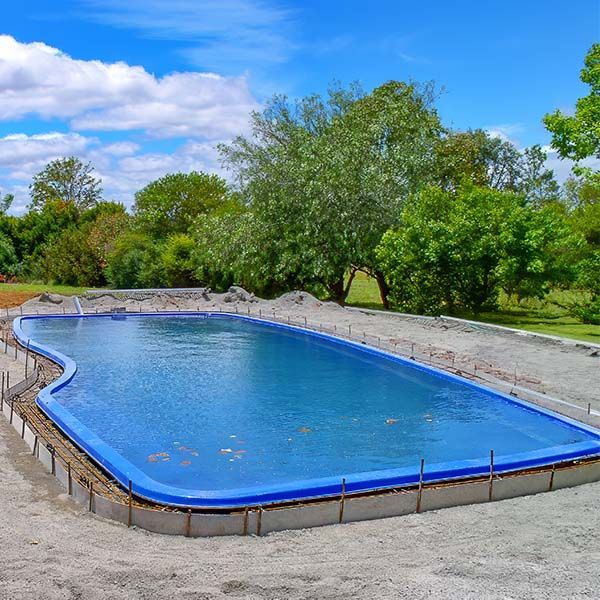 Blue empty swimming pool in a landscaped outdoor area with trees and a stone wall