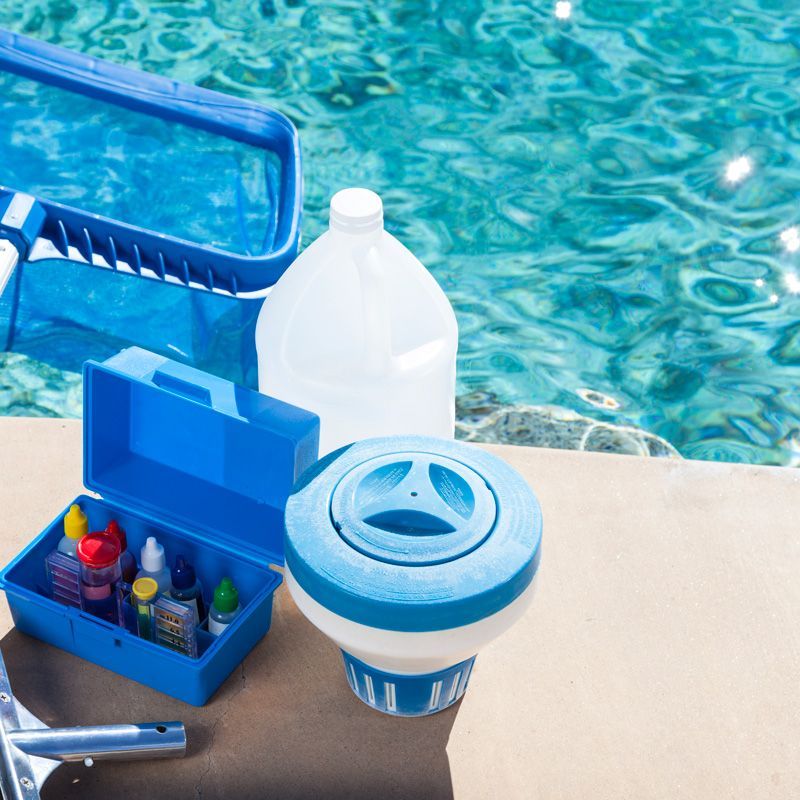 Pool cleaning supplies beside a swimming pool, including a blue caddy, bottle, and skimmer basket
