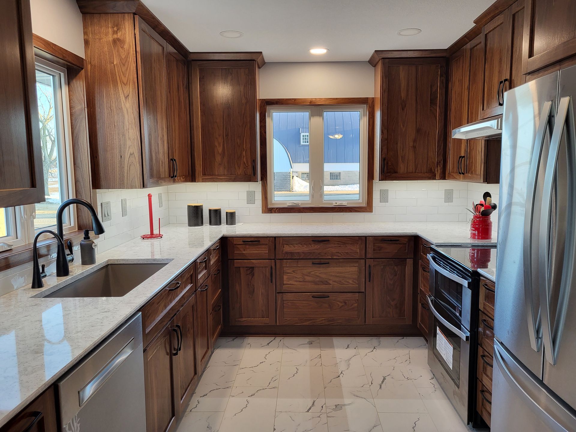 U-shaped kitchen with dark wood cabinets, stainless steel appliances, white countertops, and tiled backsplash.