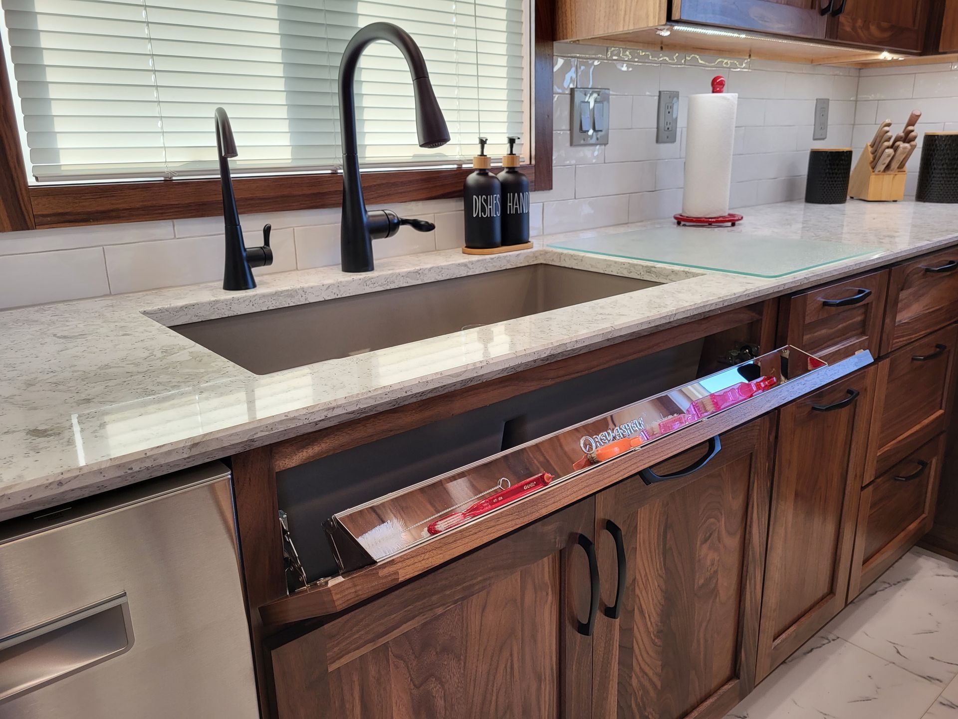 Kitchen with stainless steel sink, pull-out knife storage, dark faucet, and wood cabinetry.