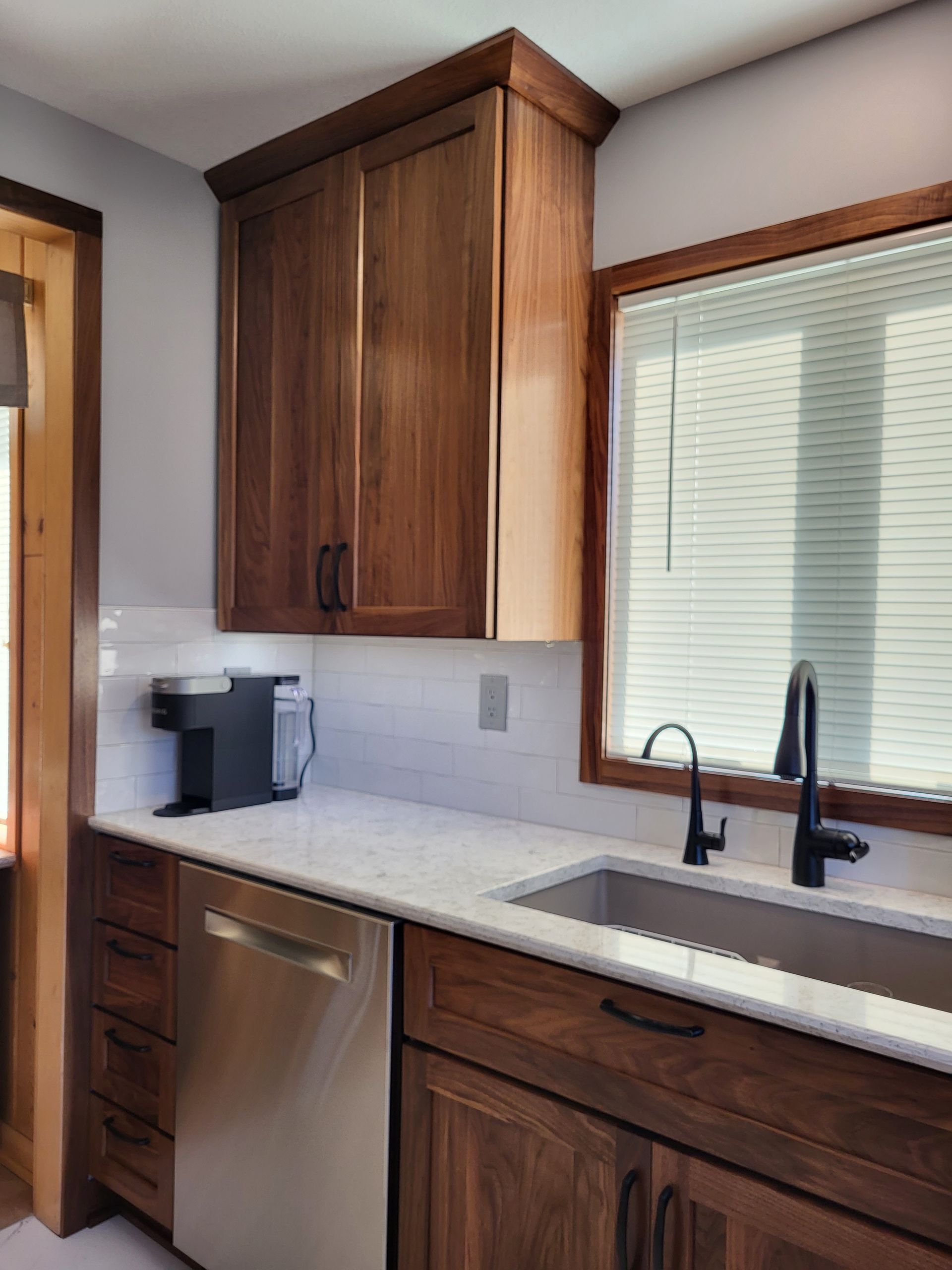 Kitchen with dark wood cabinets, stainless steel appliances, white countertops, and a window with blinds.
