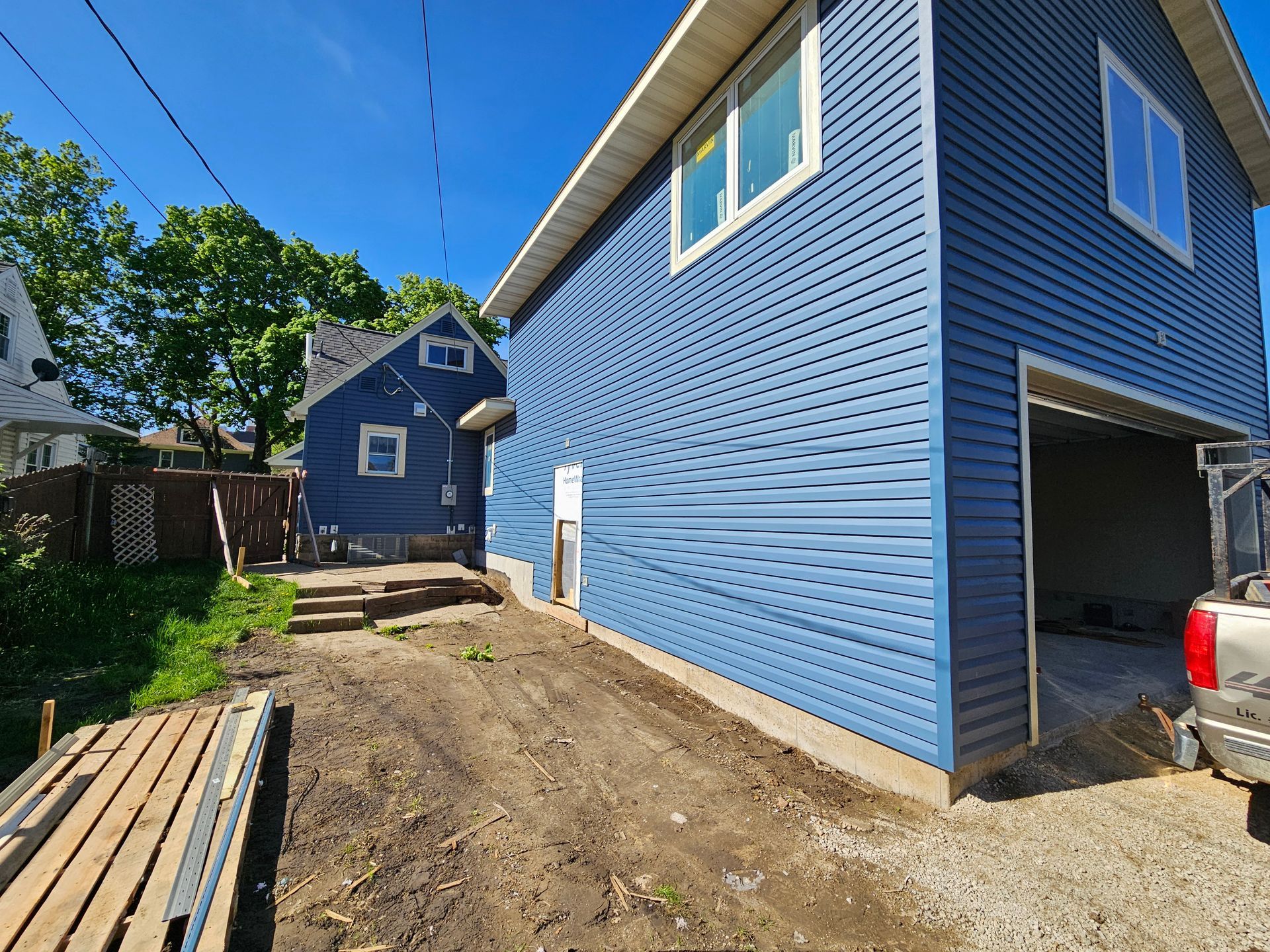 Blue house under construction with open garage and dirt driveway.