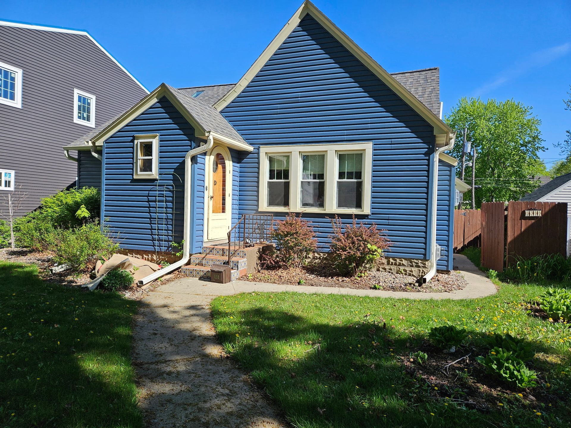 Blue house with a small yard and a sidewalk on a sunny day.