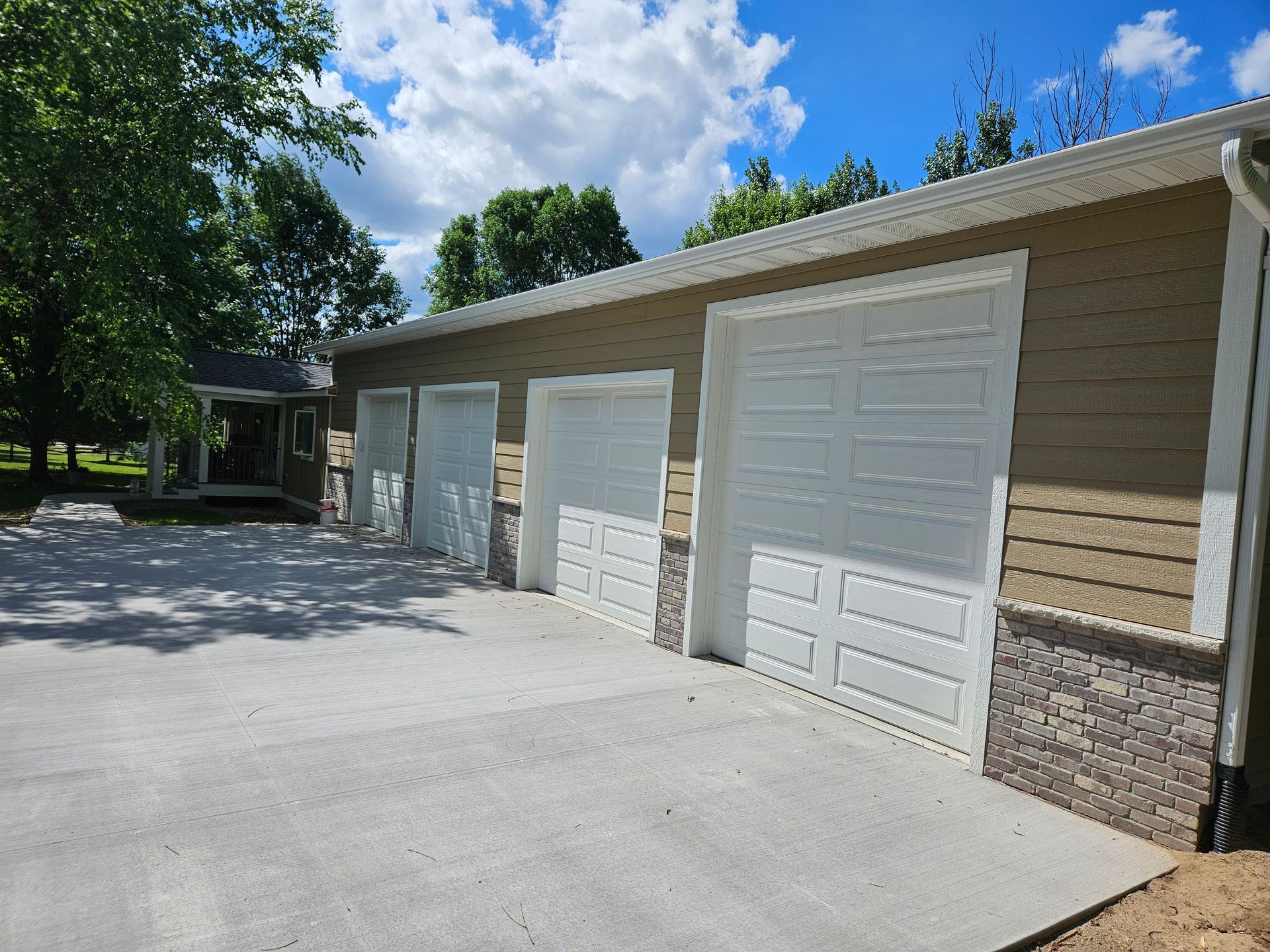 Three-car garage with white doors, tan siding, and stone accents. Concrete driveway.