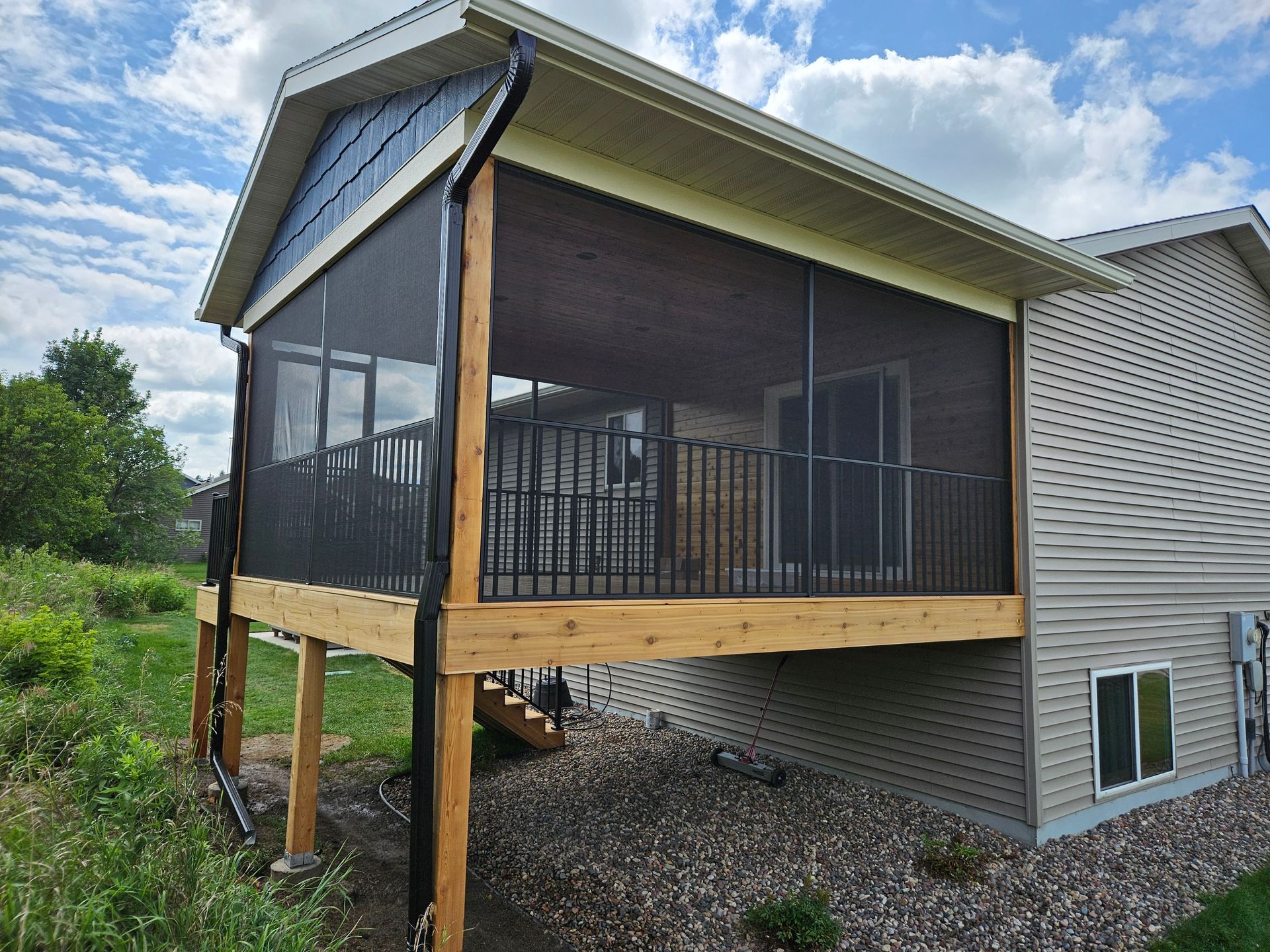Screened-in porch with black screens, wood framing, and black railing, attached to a two-story house.