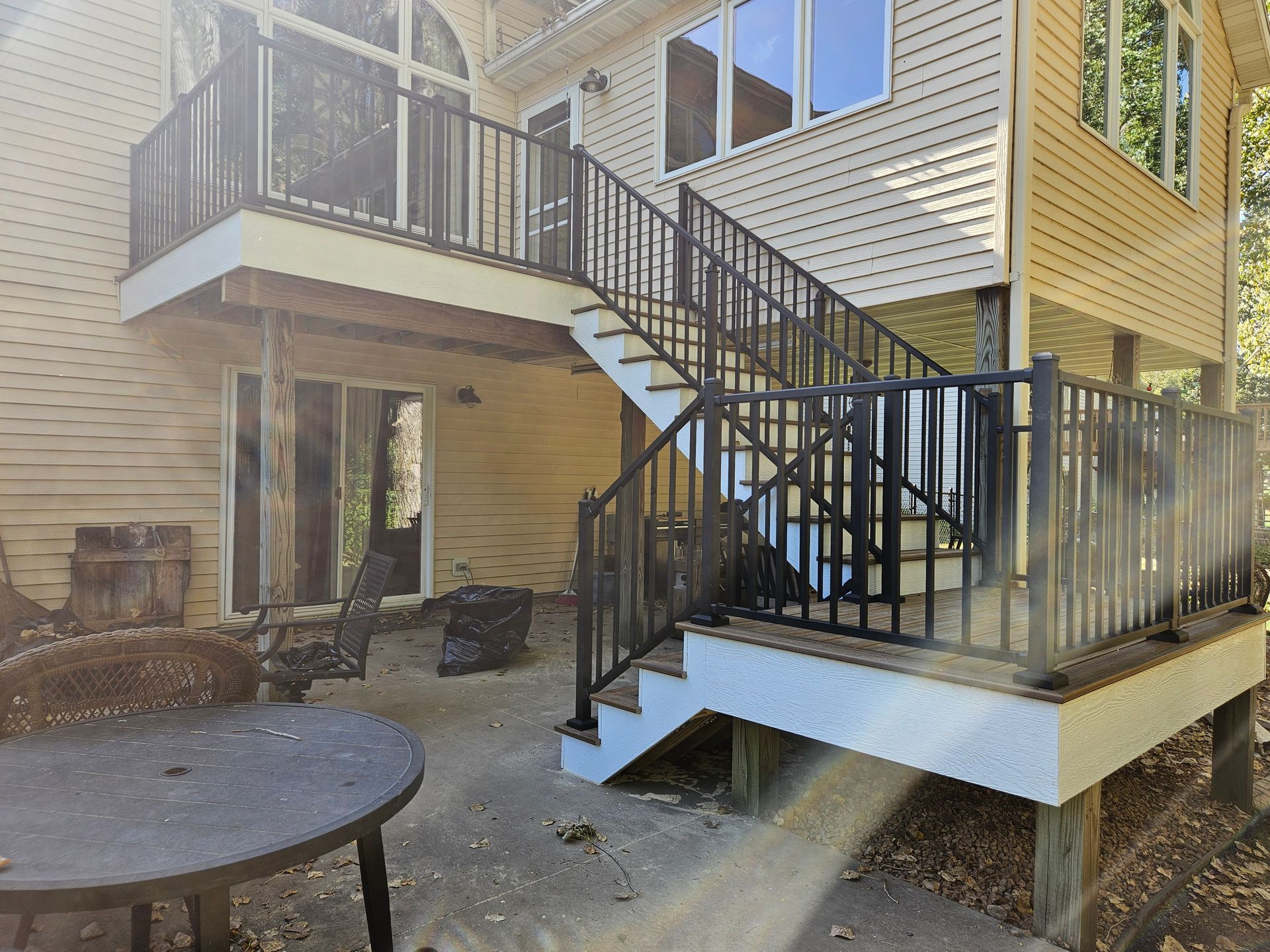 Back deck with black railings, stairs, and a patio table. Beige siding on the house.