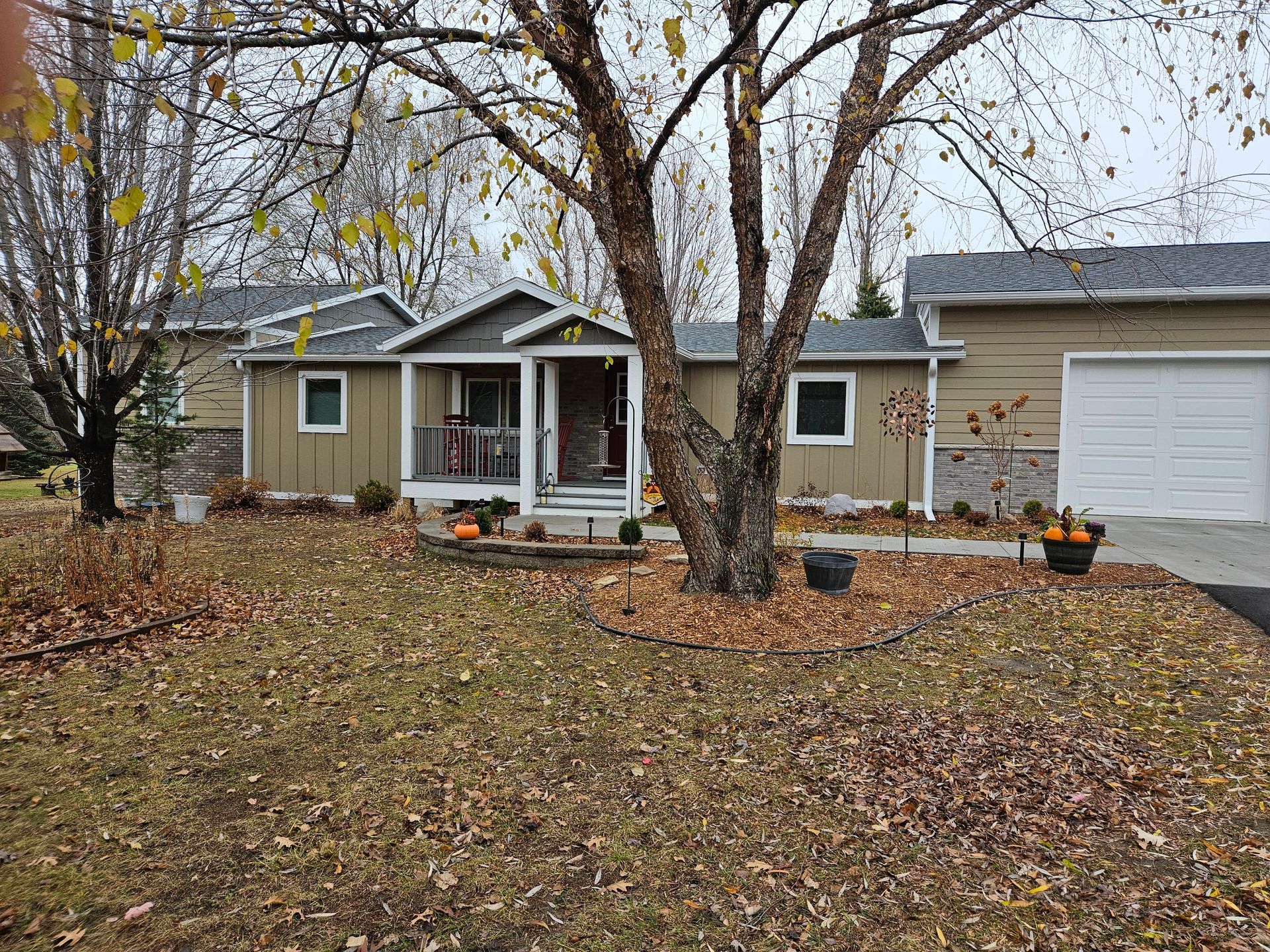 Tan house with brown roof and garage, with autumn foliage on the lawn.