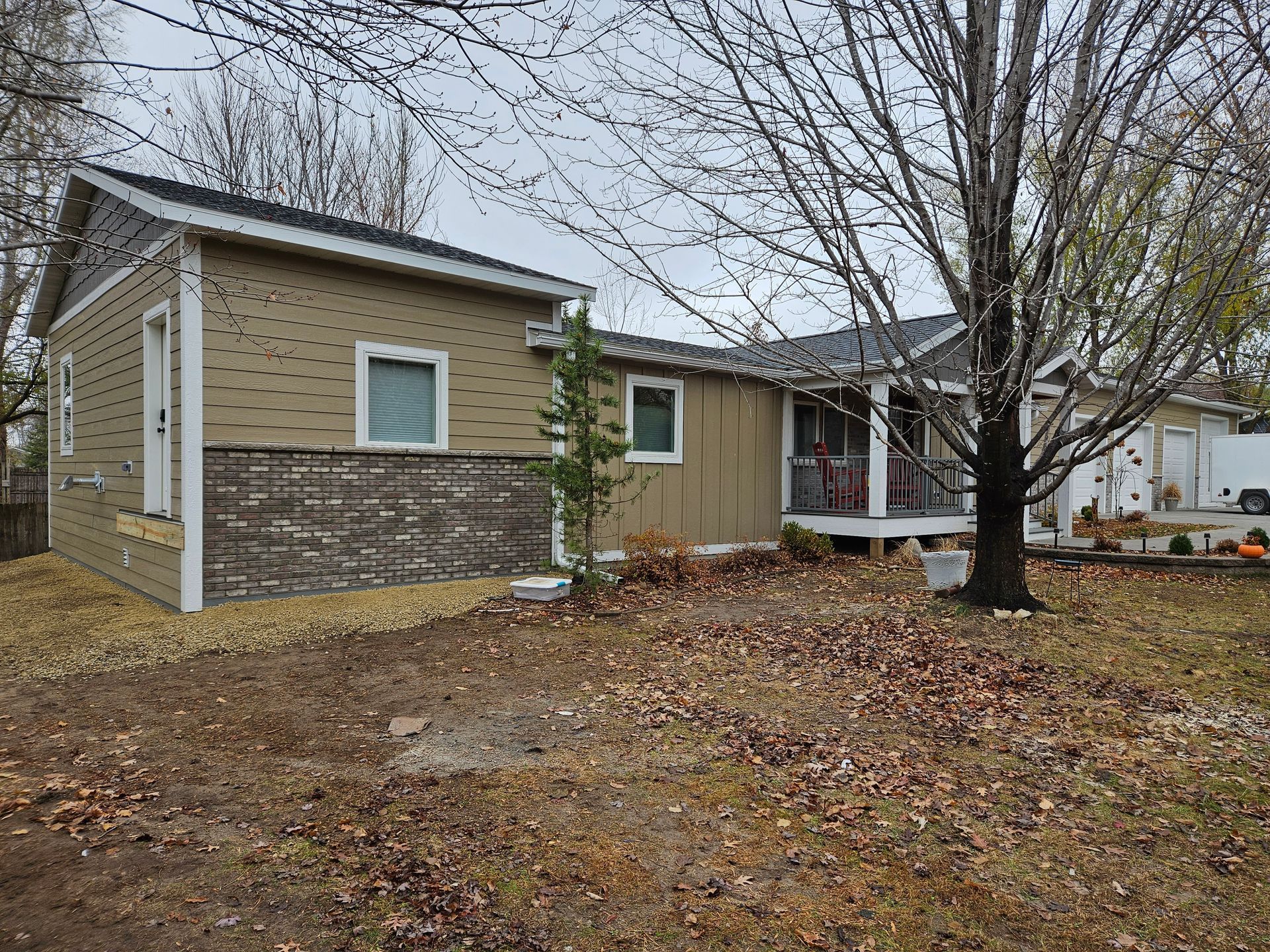 Tan house with brown siding, unfinished wall with wrapping, and a porch under a cloudy sky.