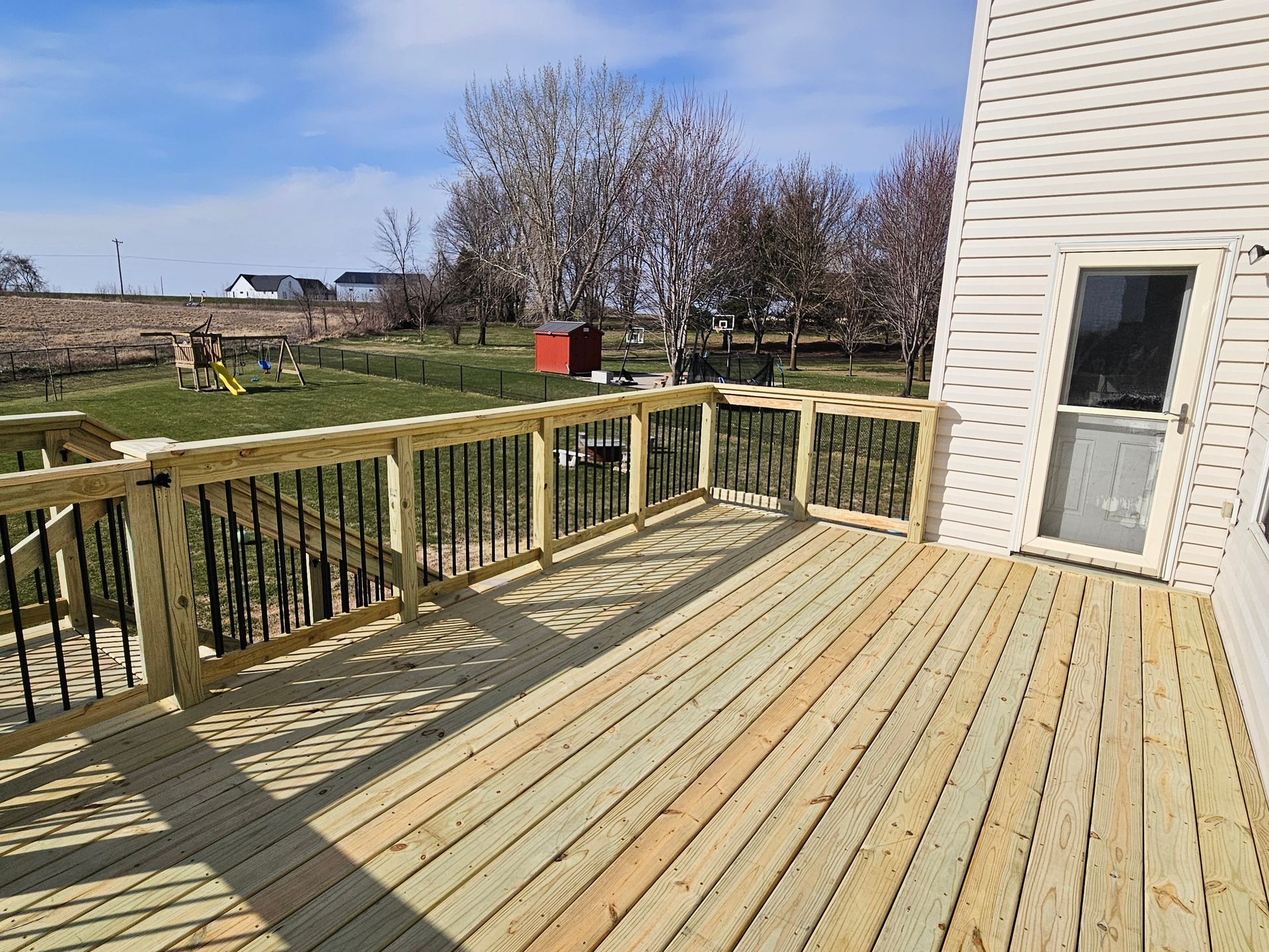 New wooden deck with black railing and a door, viewed from above on a sunny day.