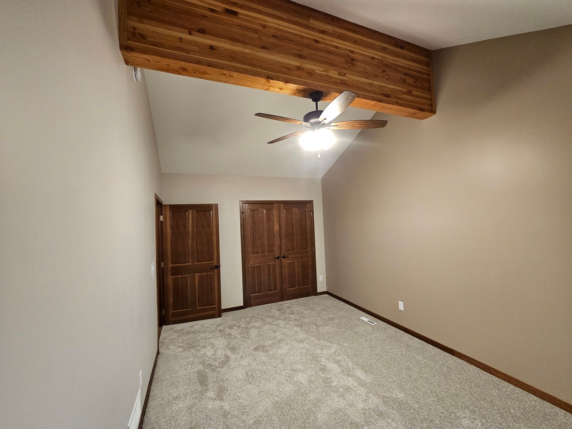Bedroom with vaulted ceiling, wooden beam, carpet, and two wood doors.