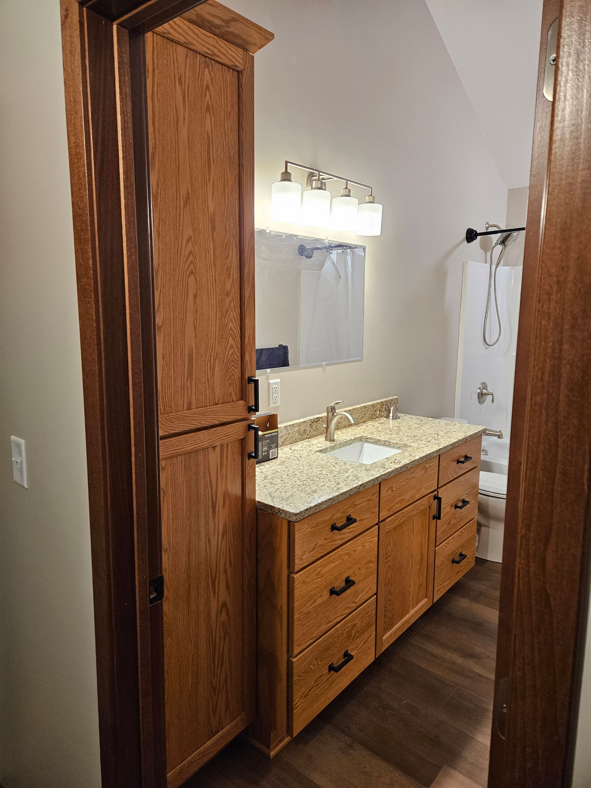 Bathroom with wood cabinets, granite countertop, and a tall storage cabinet.