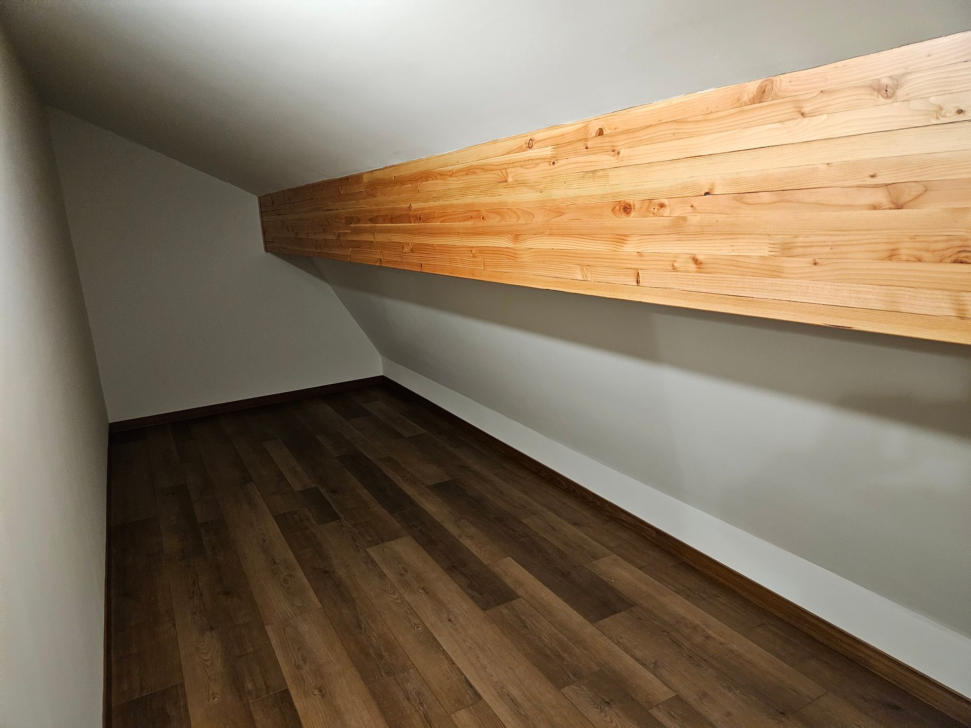 An attic-like room with dark wood floor, white walls, and a wooden beam overhead.