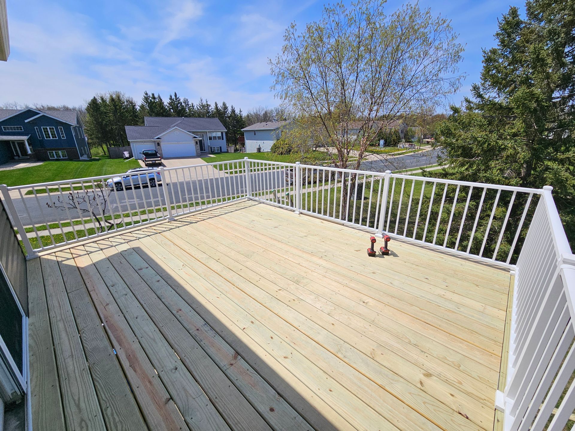 Wooden deck with white railing, overlooking a suburban neighborhood on a sunny day.