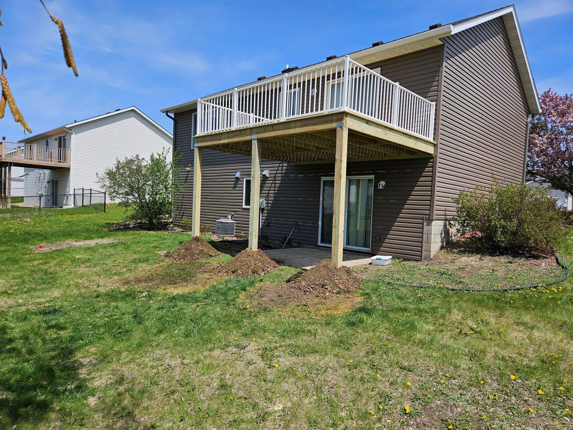 A two-story house with a wooden deck on the second level, brown siding, and a grassy yard.