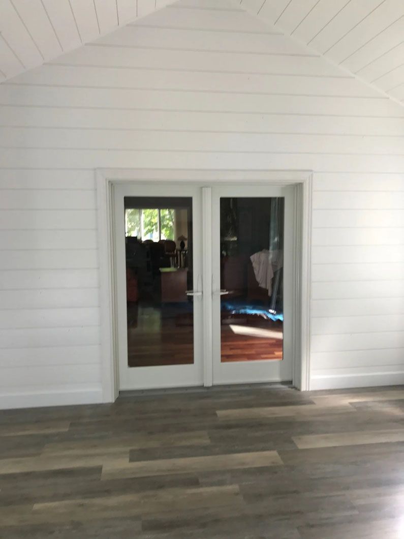 White-walled room with glass doors and wood-look flooring. Interior view with a peek of the outside.
