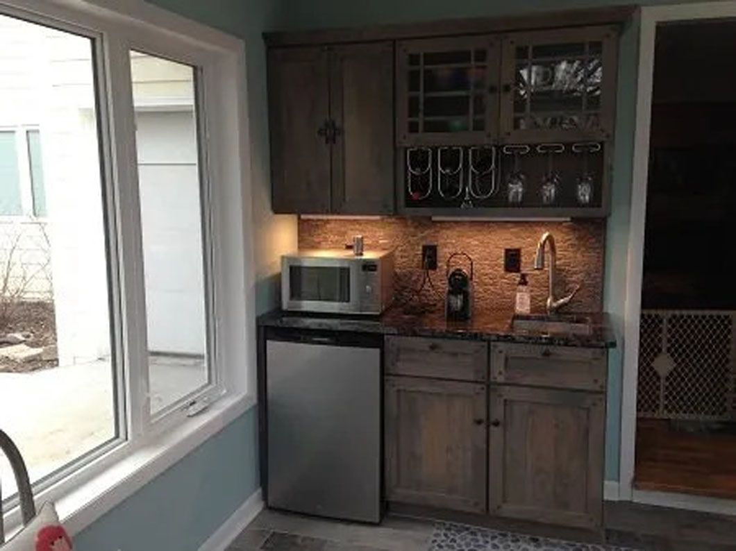 Mini kitchen with cabinets, sink, microwave, and mini-fridge, in a room with a window.