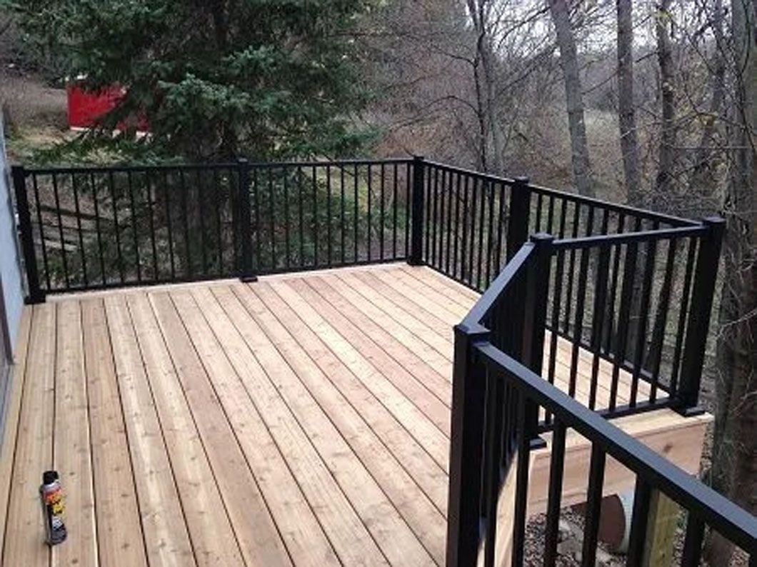 Wooden deck with black railing overlooking a wooded area.