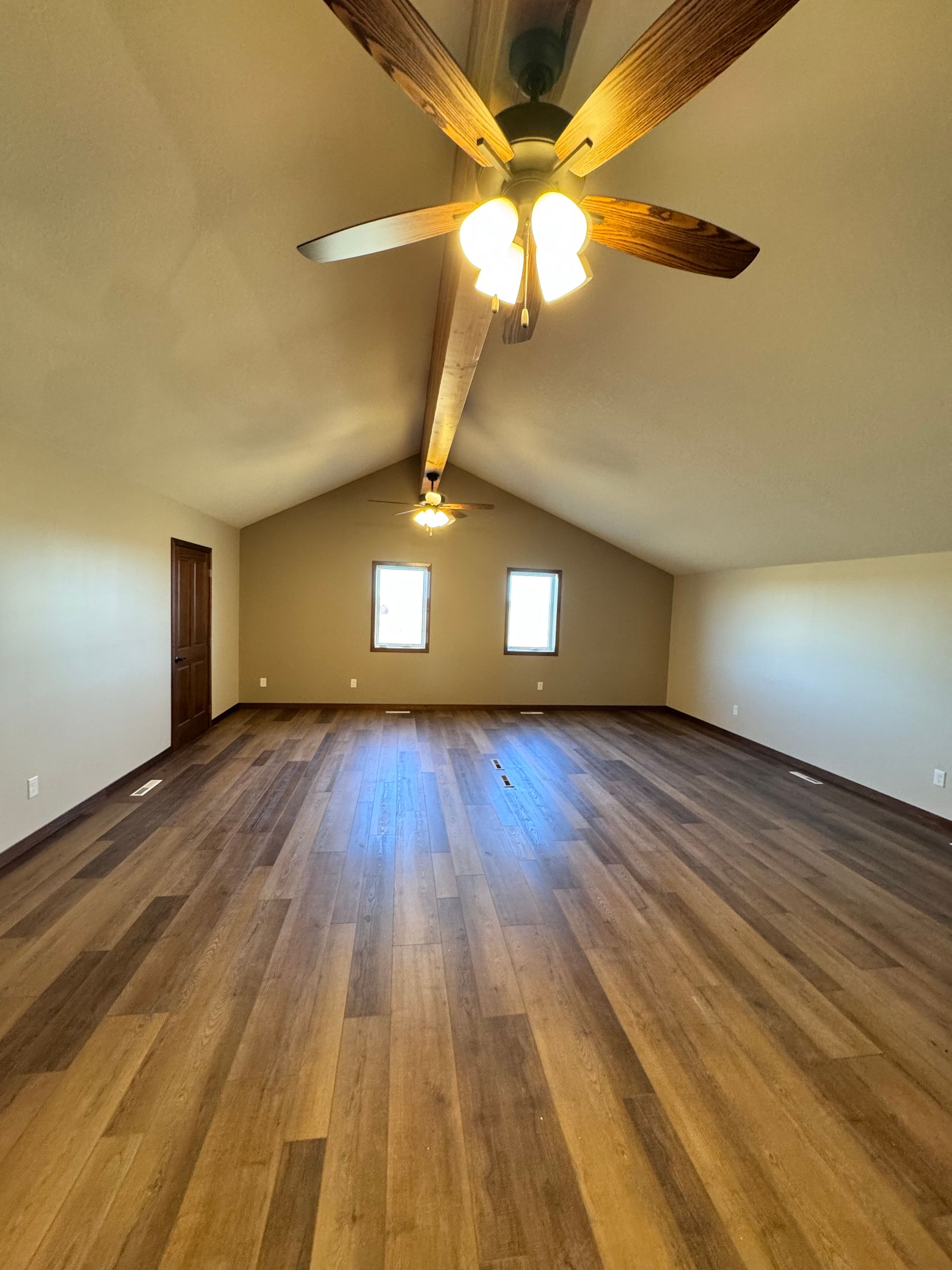 Spacious room with wood floor and sloped ceiling. Ceiling fan, small windows, and neutral walls.