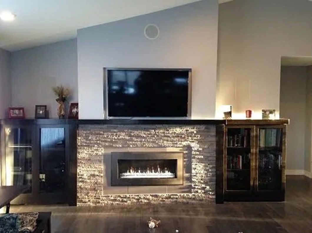 Fireplace with built-in TV, cabinets, and brick-style tile in a living room with dark wood floors.