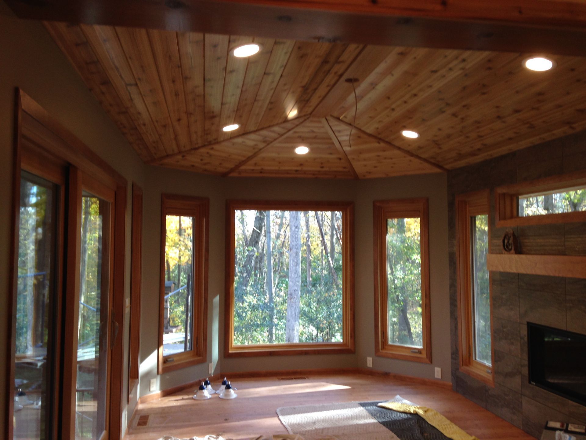 Sunroom with wood ceiling and windows overlooking trees.