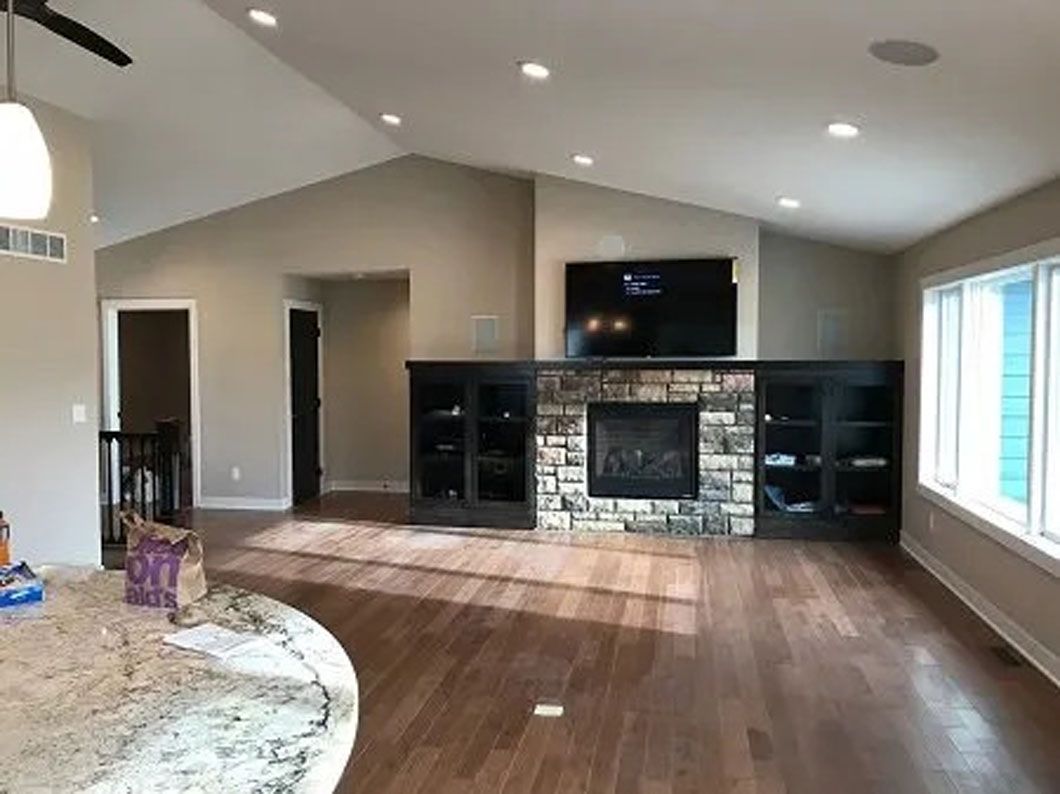 Living room with hardwood floors, fireplace, TV, black cabinets, and a high ceiling.