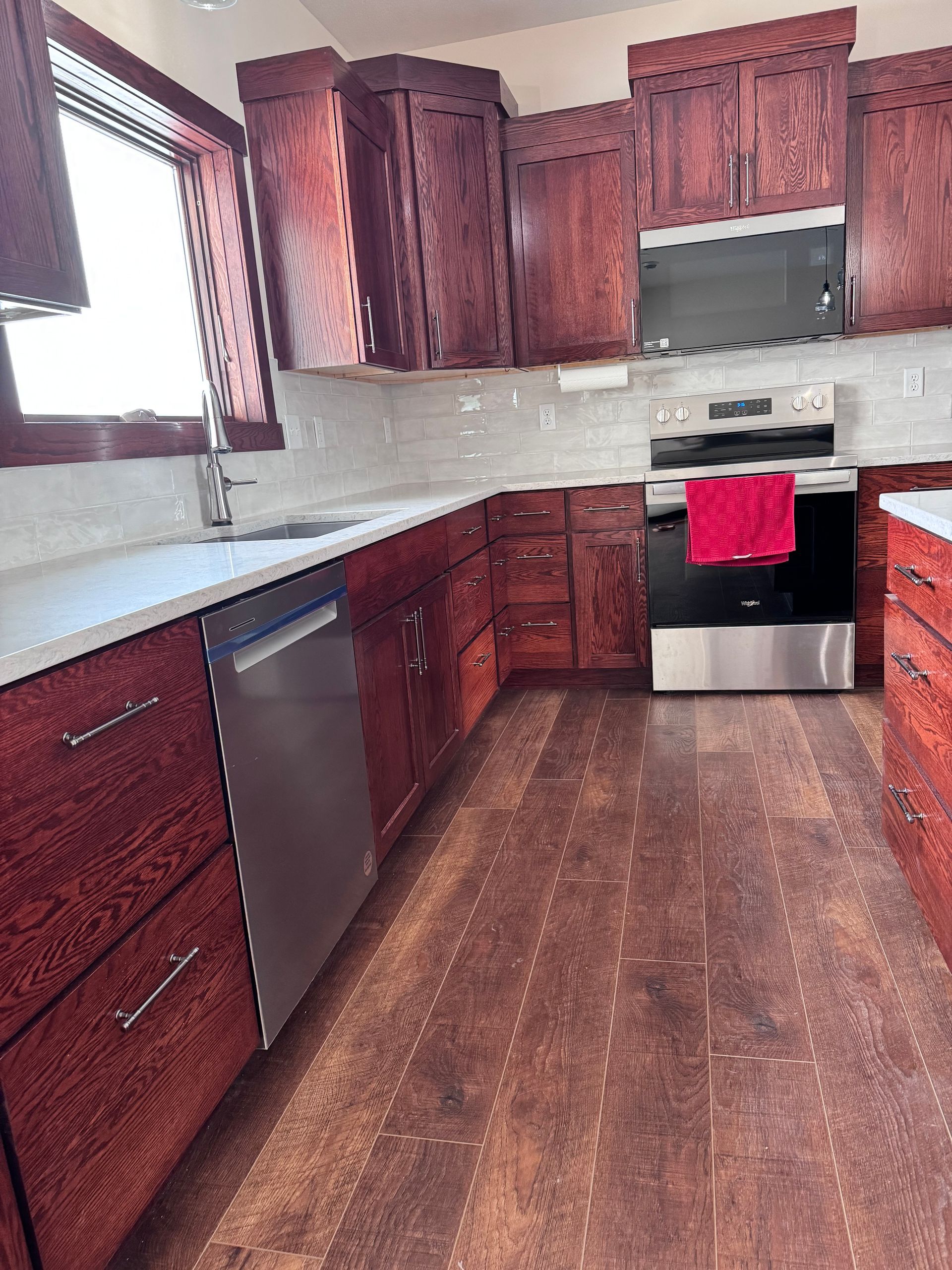 Kitchen with dark red cabinets, stainless steel appliances, and wood flooring.