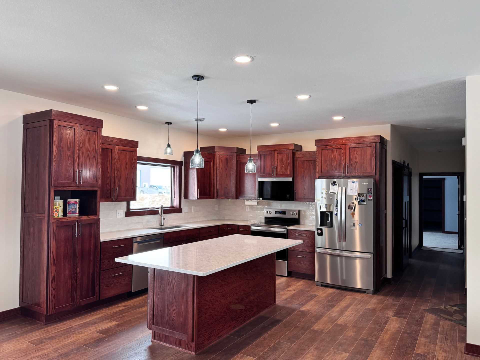 Red-toned kitchen with dark wood cabinets, stainless steel appliances, and a white island.