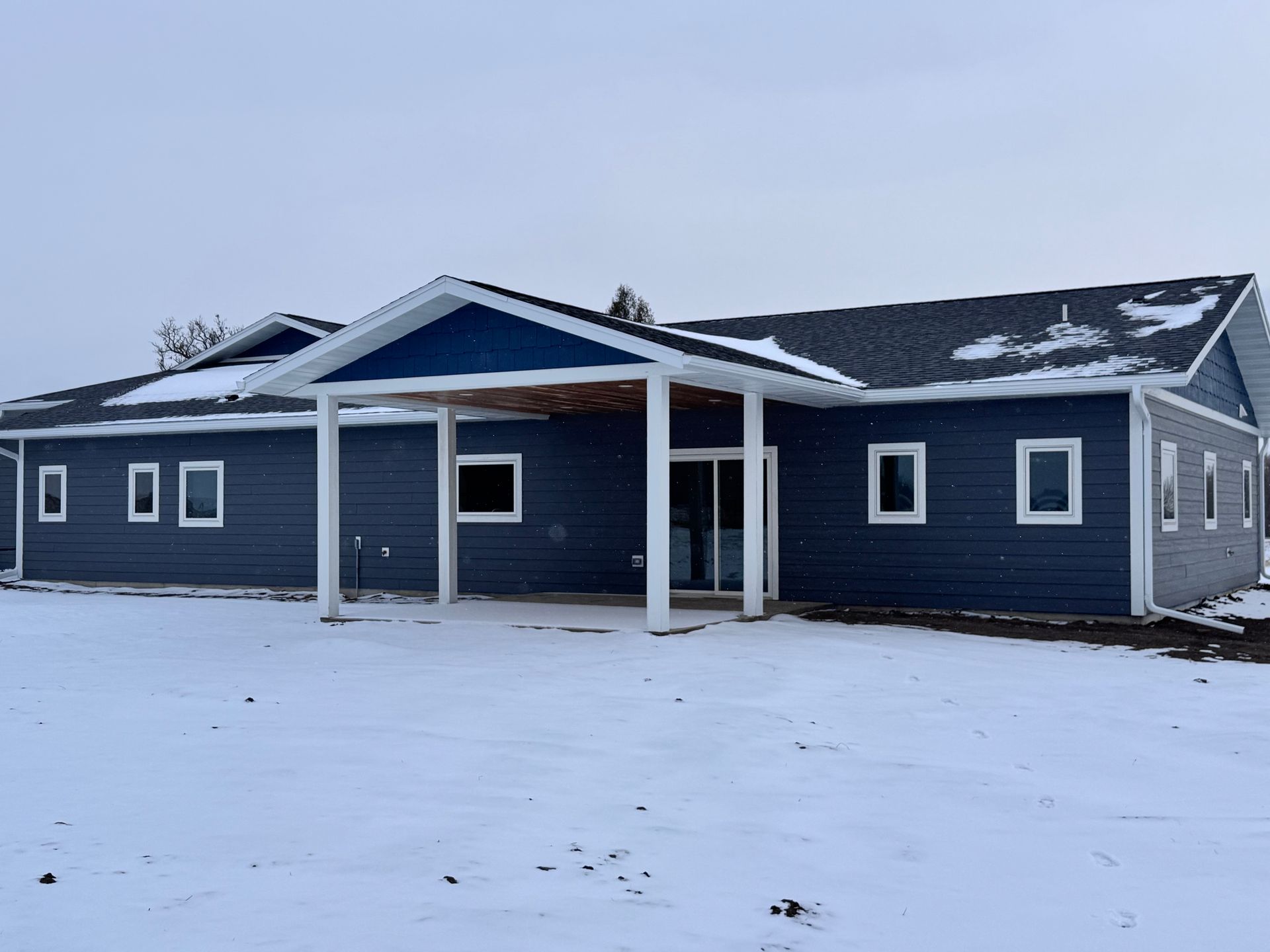 Blue building with white trim and a covered entrance in a snowy field.